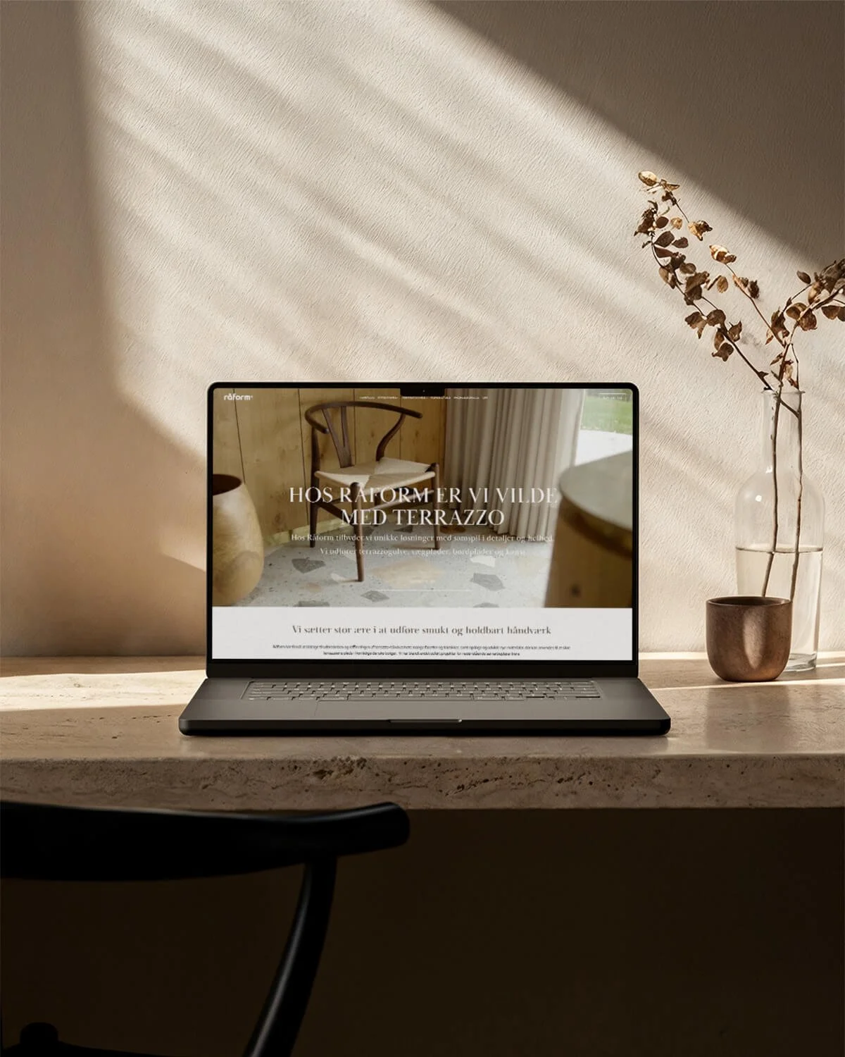 Laptop på bord med hjemmeside designet for Råform, om terrazzo, i et rum med sollys, planter og bord.