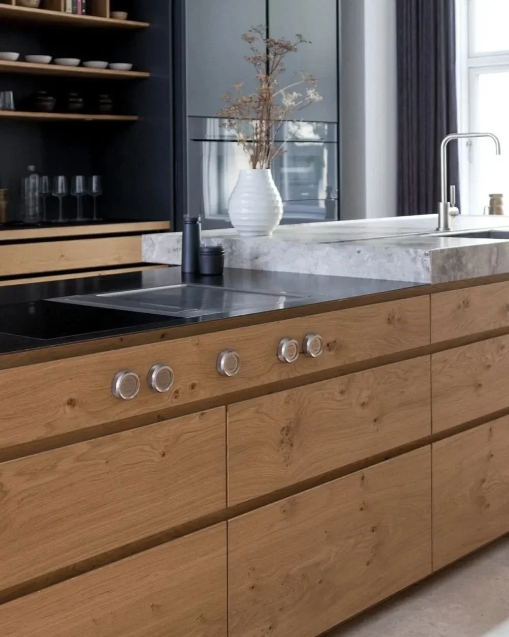 Reference fra hjemmeside design med et billede af et moderne boform køkken med træskabe, sort komfuret, en balance med fire knapper, en vask med rustfrit stålforsyningshane, en hvid vase med tørret blomster, og en stor vindue med gardiner.