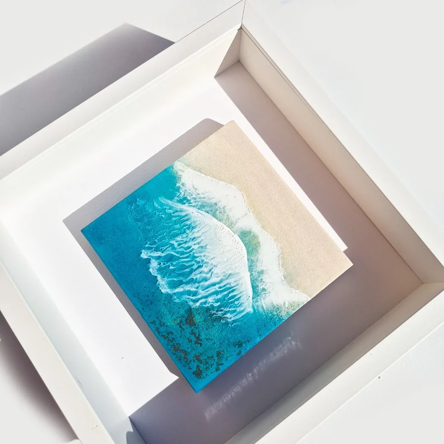 Framed square resin artwork of an ocean wave, with real sand and deep blue water details, by Irish artist Orla Doyle.