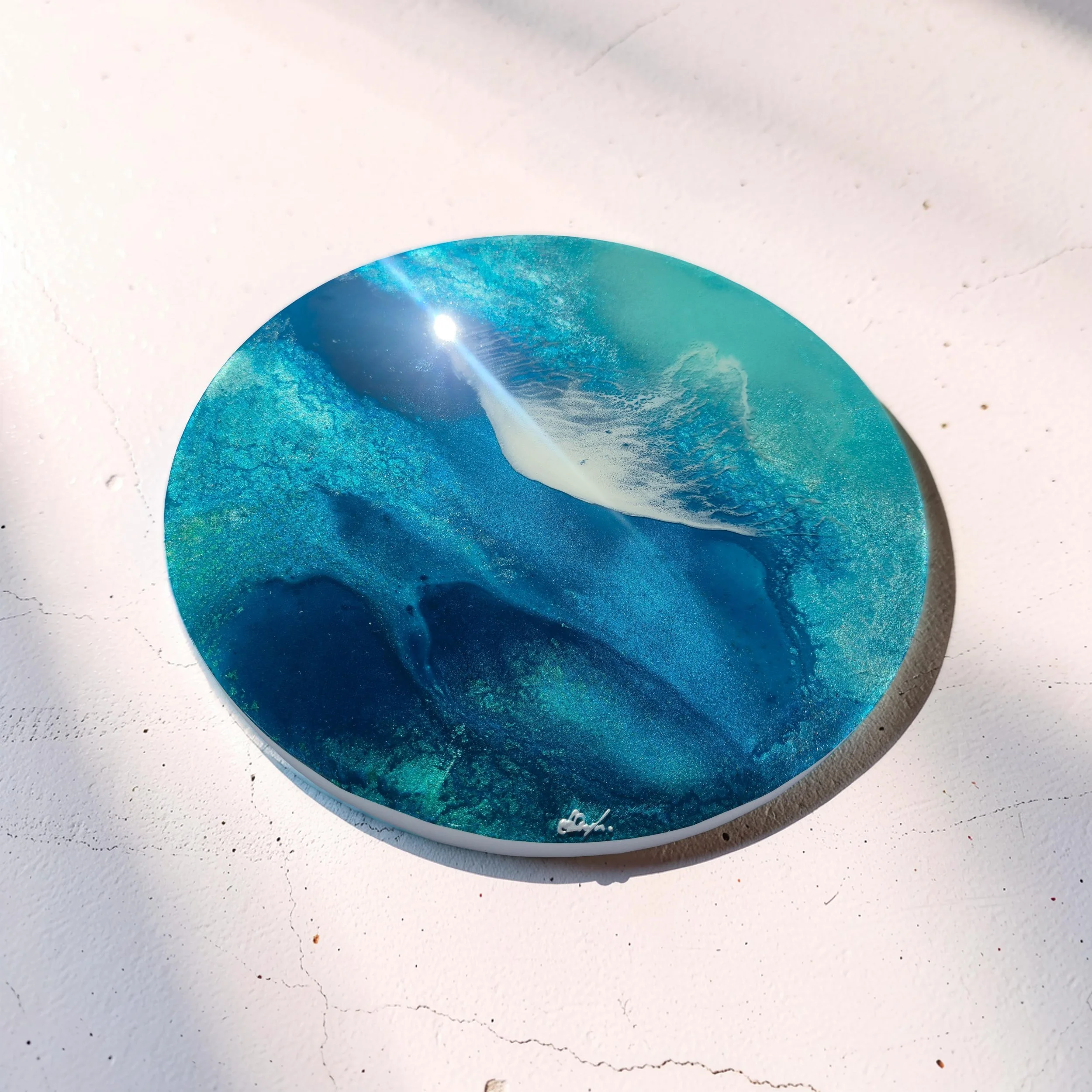 Easy Tide round resin artwork on a soft pink wall surface. Aerial ocean composition with depth and shimmer.