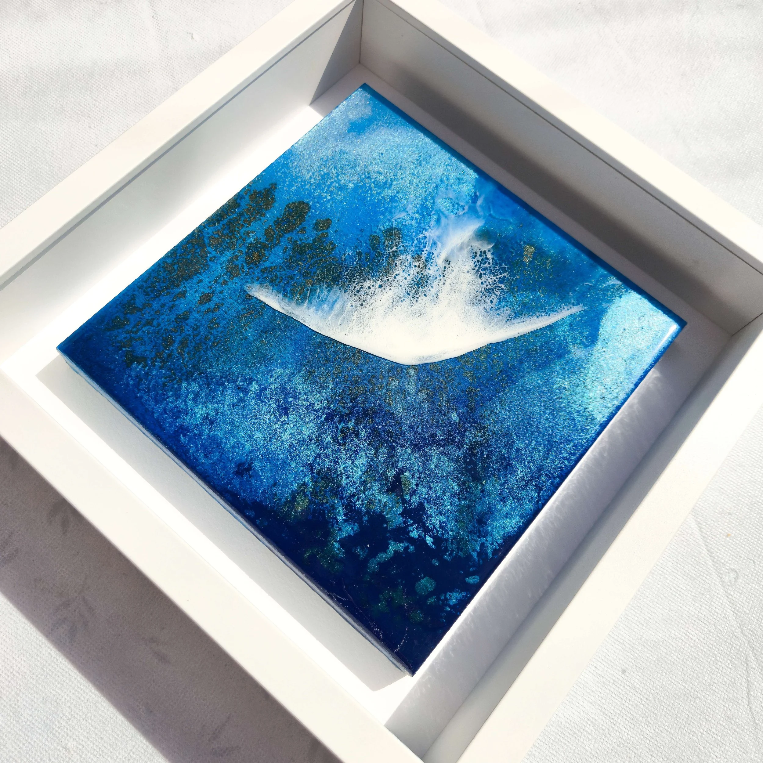 Framed resin artwork titled Silver Springs showing white flowing water form across deep blue ocean tones with gold speckles.