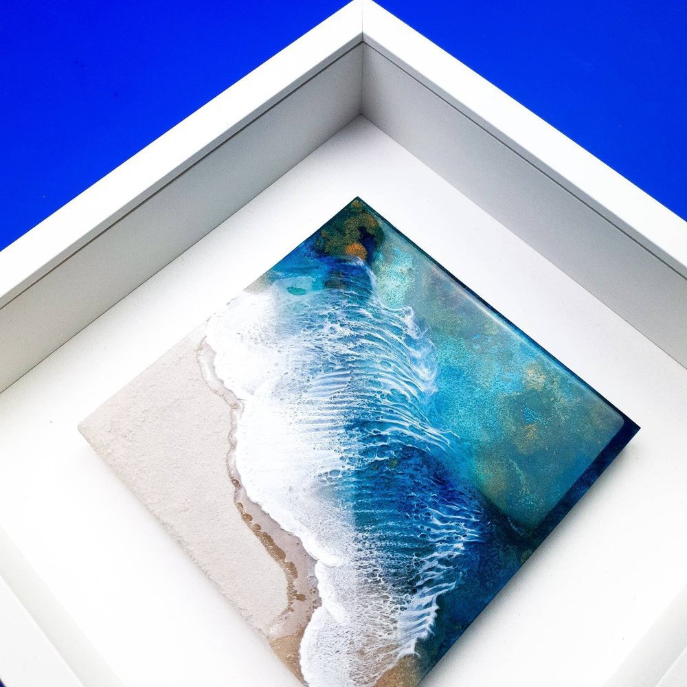 Close up of ocean-inspired resin painting with blue and real sand capturing realistic beach beauty.
