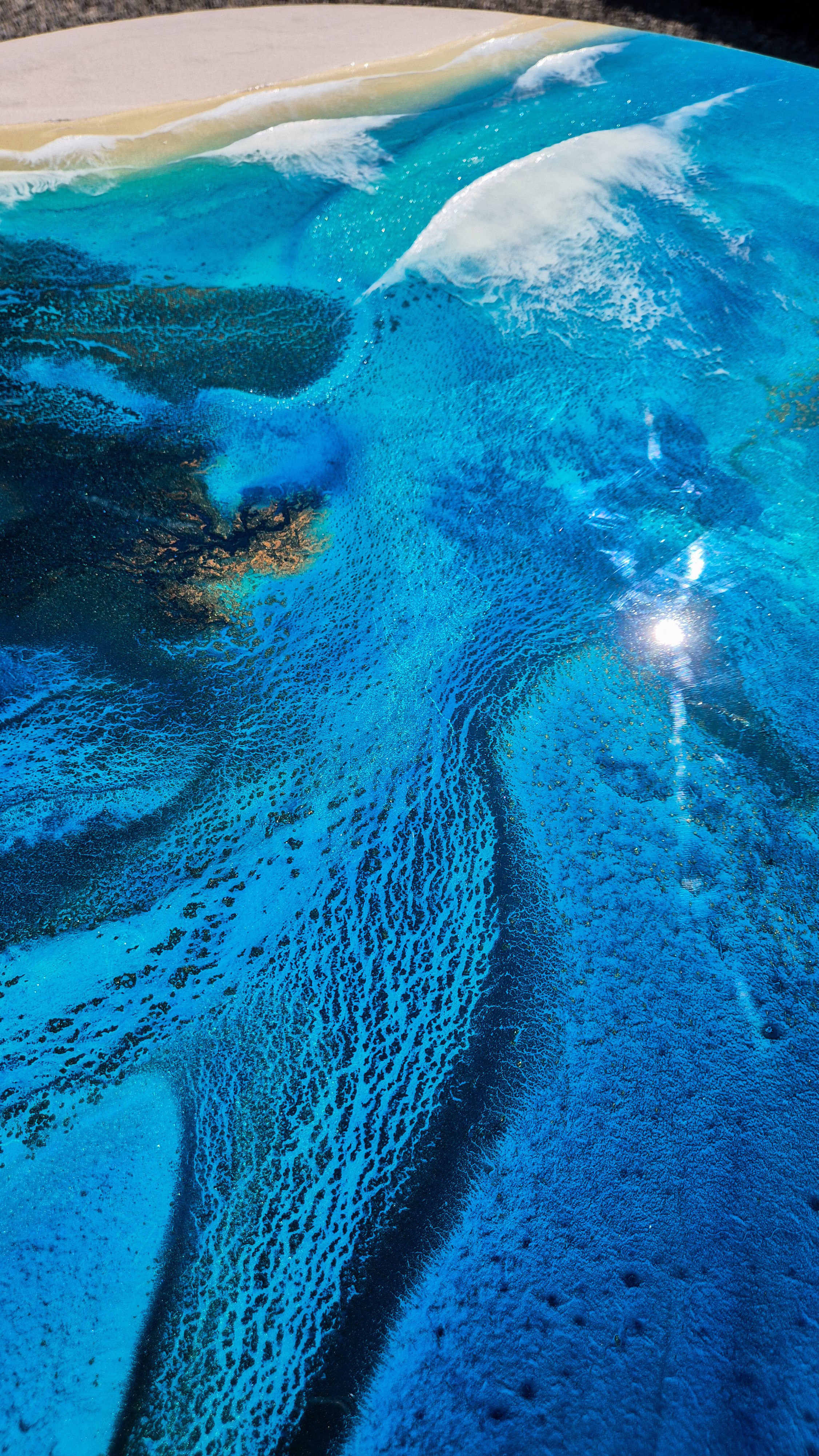 Large round resin artwork with swirling blue ocean textures and sandy shoreline, featuring a high-gloss finish on wood panel.