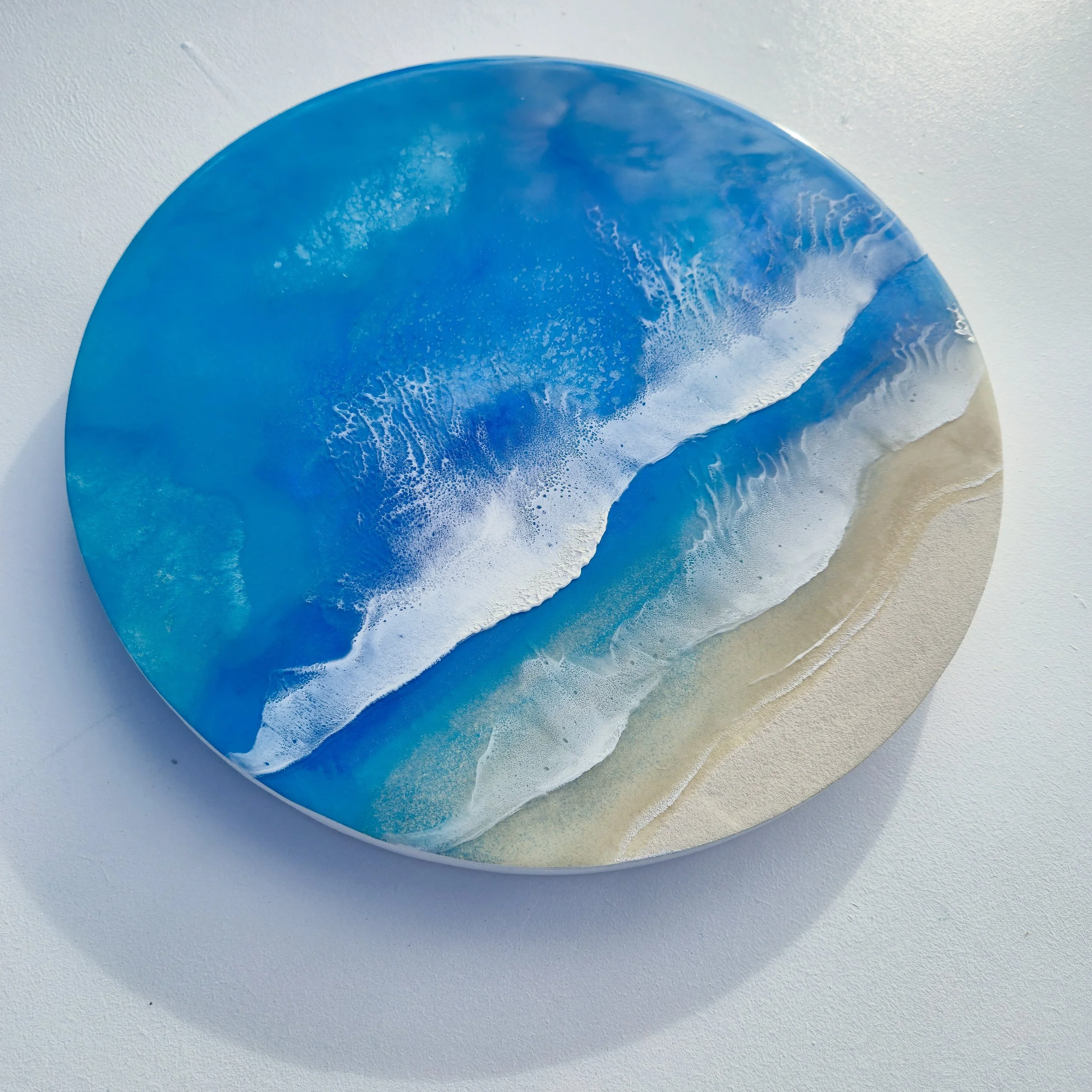 Round resin artwork featuring turquoise ocean water, two white foam wave bands, and sandy shoreline in realistic detail.