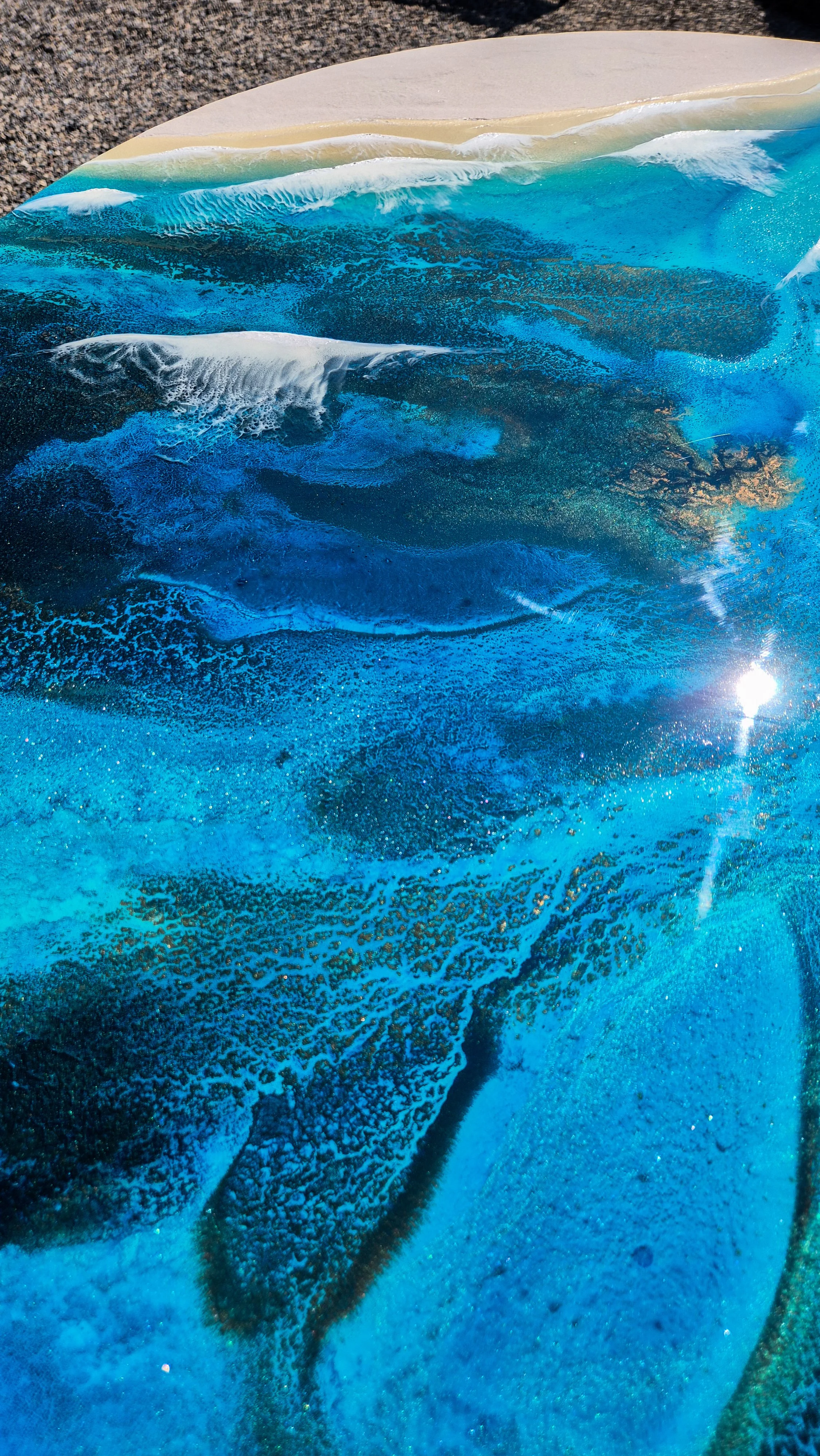 Large round resin artwork with swirling blue ocean textures and sandy shoreline, featuring a high-gloss finish on wood panel.