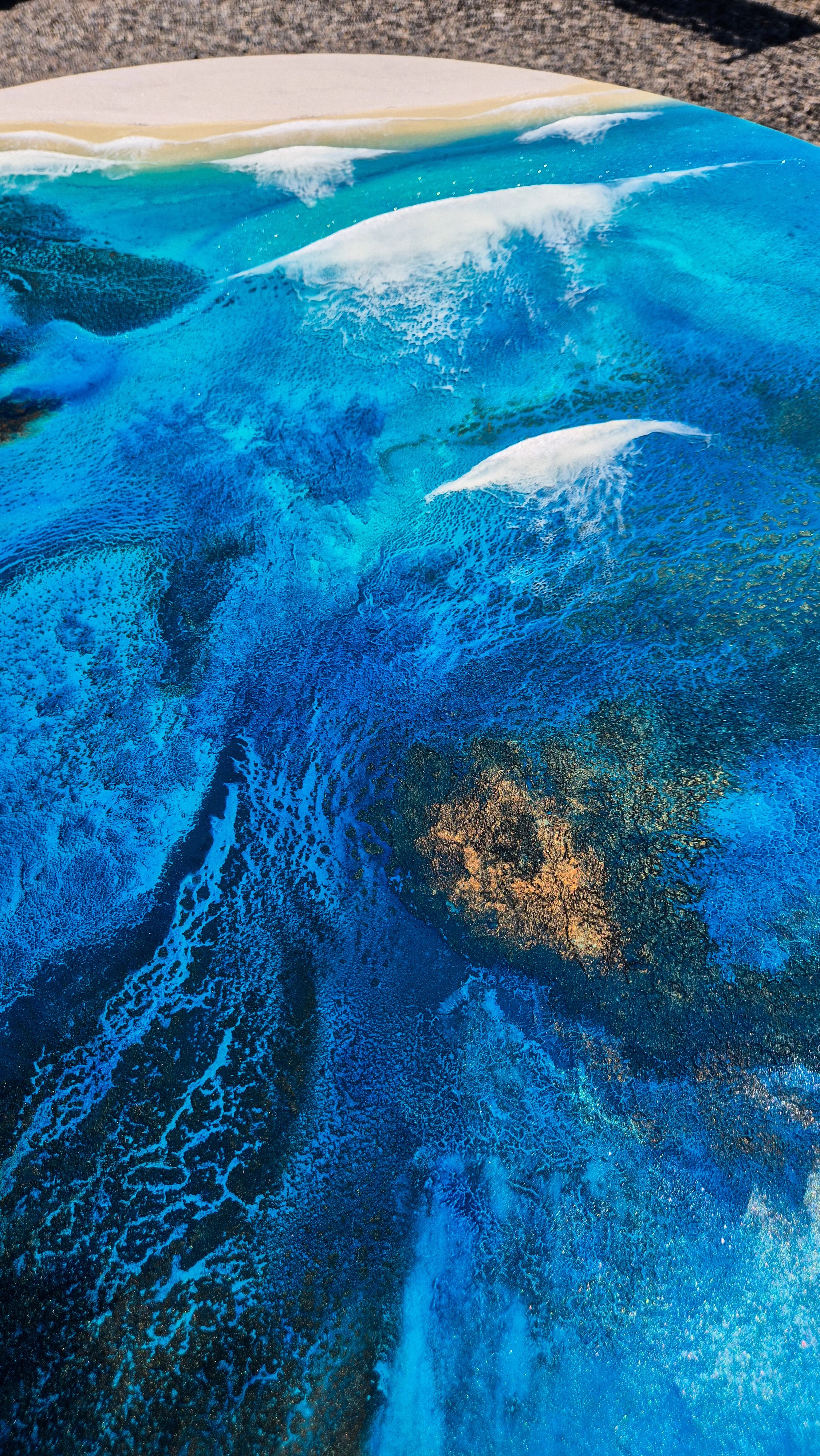Large round resin artwork with swirling blue ocean textures and sandy shoreline, featuring a high-gloss finish on wood panel.