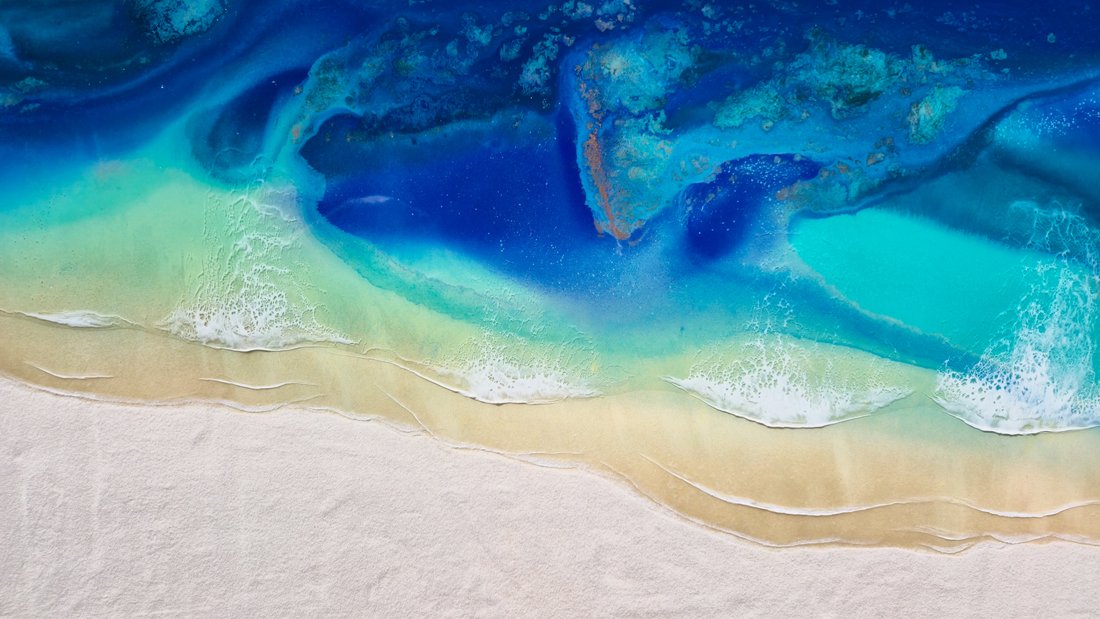 Handmade resin ocean artwork titled “Ocean Reverie” with real sand, hanging above a modern white sofa in a bright living room.