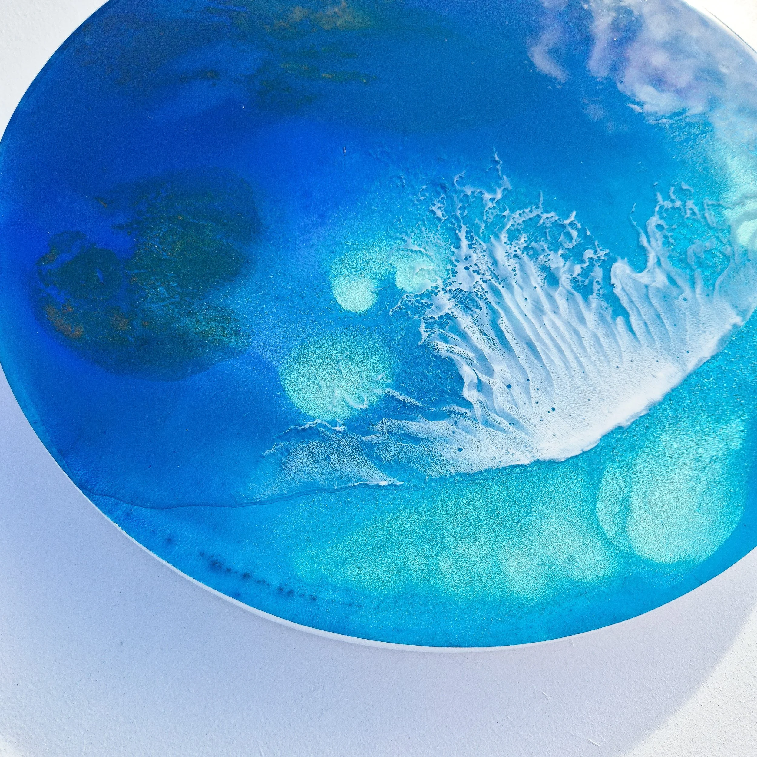 Round resin artwork with gradient blues, turquoise, and white foam texture, inspired by sunlight through ocean water.