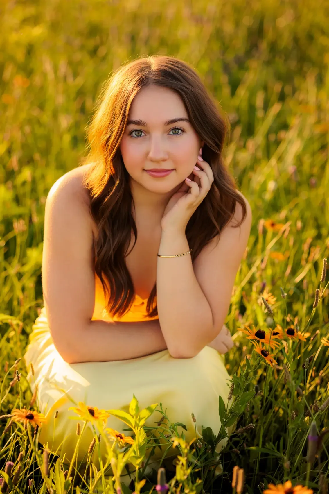Senior girl in a yellow dress sitting in a field of orange and yellow flowers during sunset, at Water Works Park in Des Moines.