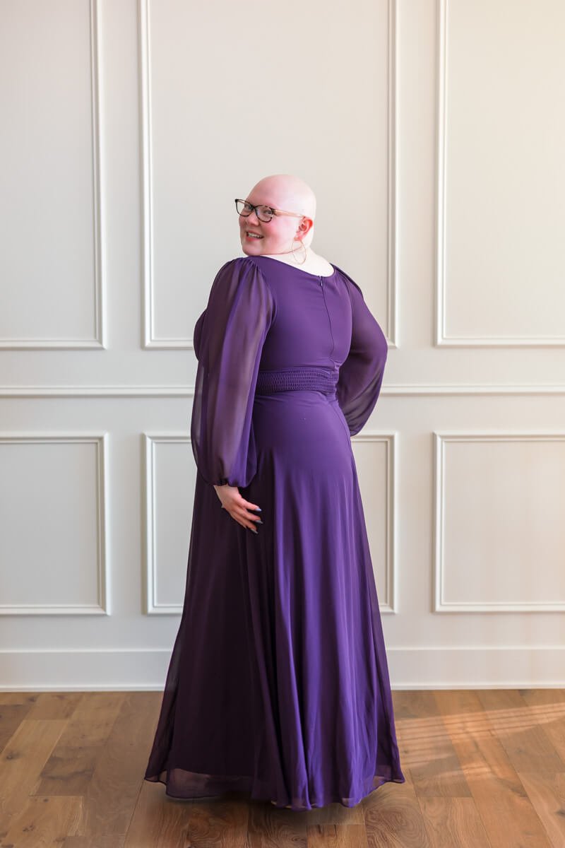 Senior girl wearing glasses showing the back of her purple prom dress in Des Moines.