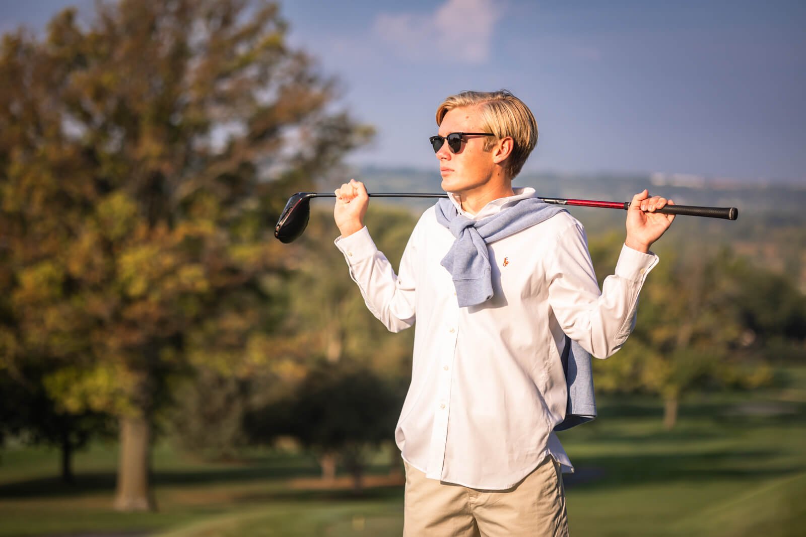 Senior boy holding golf club behind his shoulders, looking off to the side.