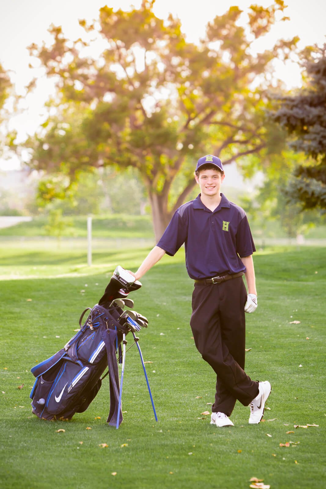 Senior boy wearing his school golf uniform, standing next to his golf bag.