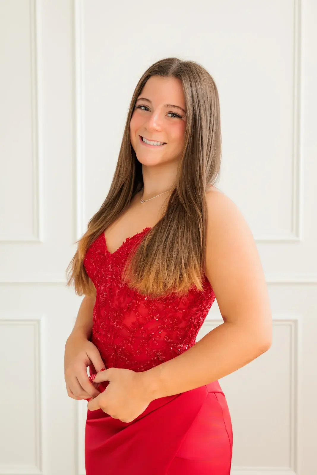 Close up of senior girl with long hair wearing a red prom dress with sequins on the bodice.