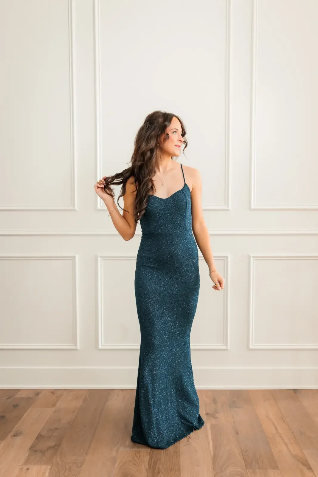 Senior girl wearing a dark green/teal prom dress, playing with her hair.  Photo by Wendy Sorensen, a Des Moines senior photographer.