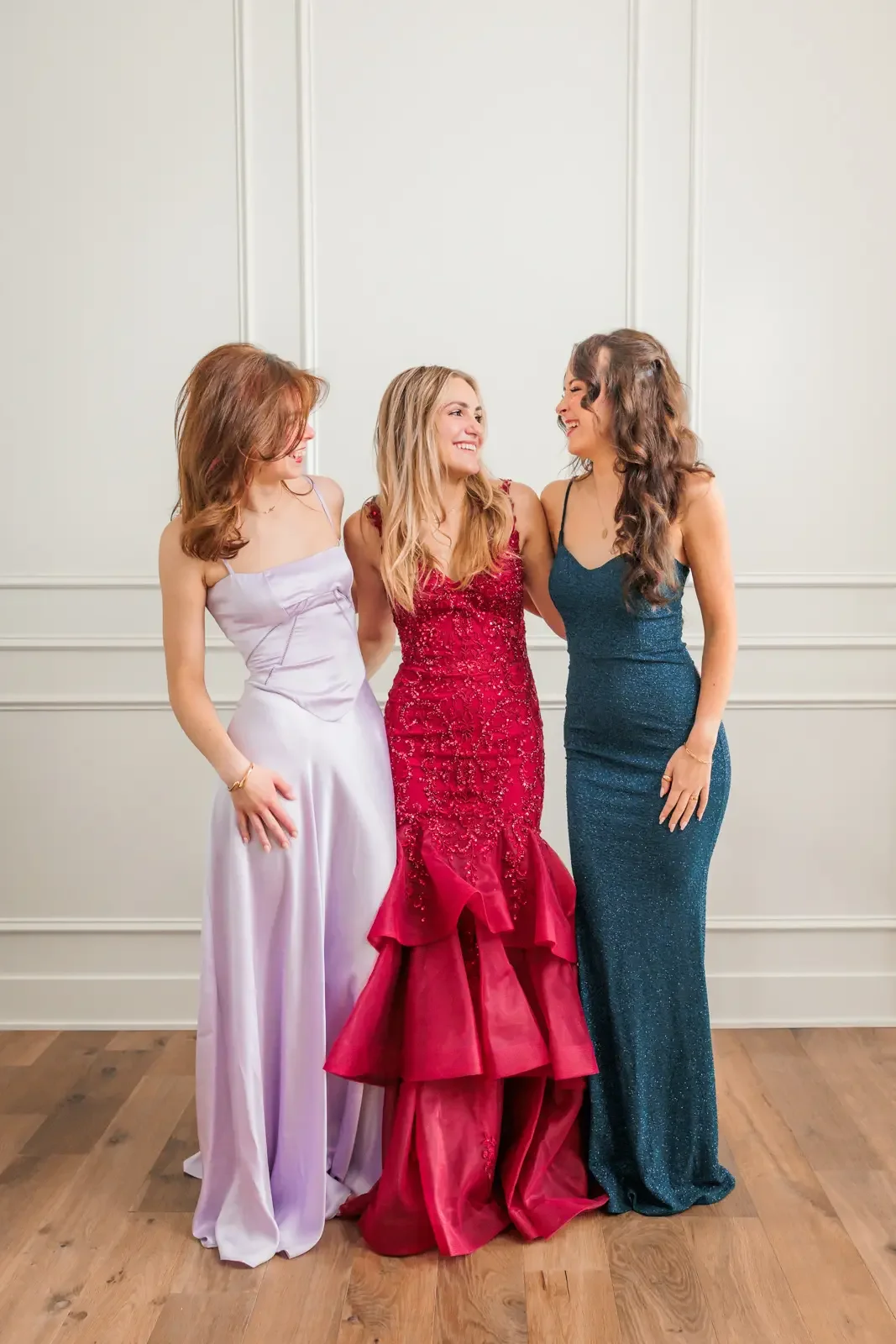 Three friends smiling and laughing together, modeling their prom dresses.