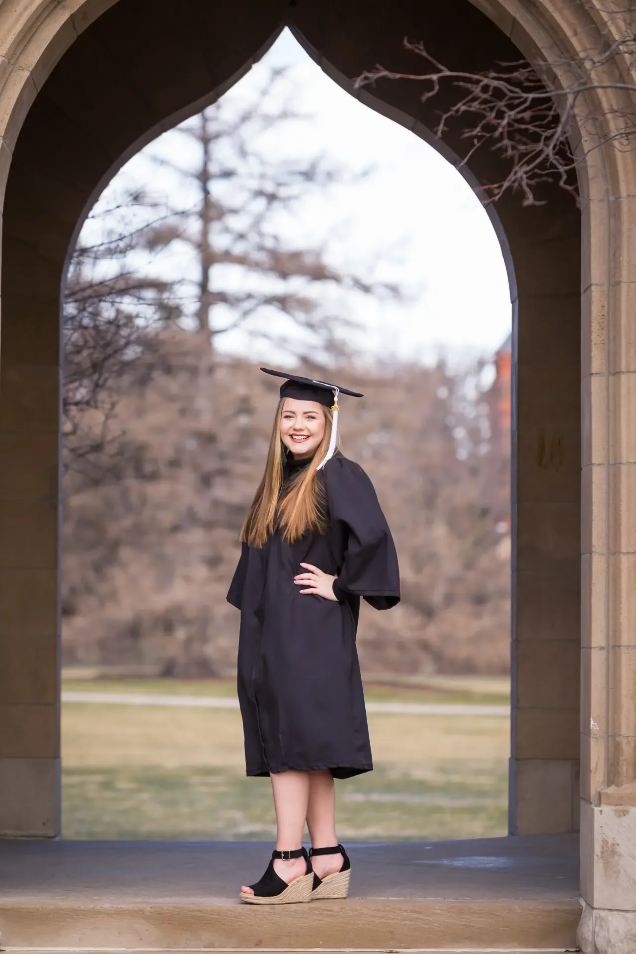 Close-up of senior girl with long blonde hair wearing graduation cap and gown at Iowa State's Campanile.