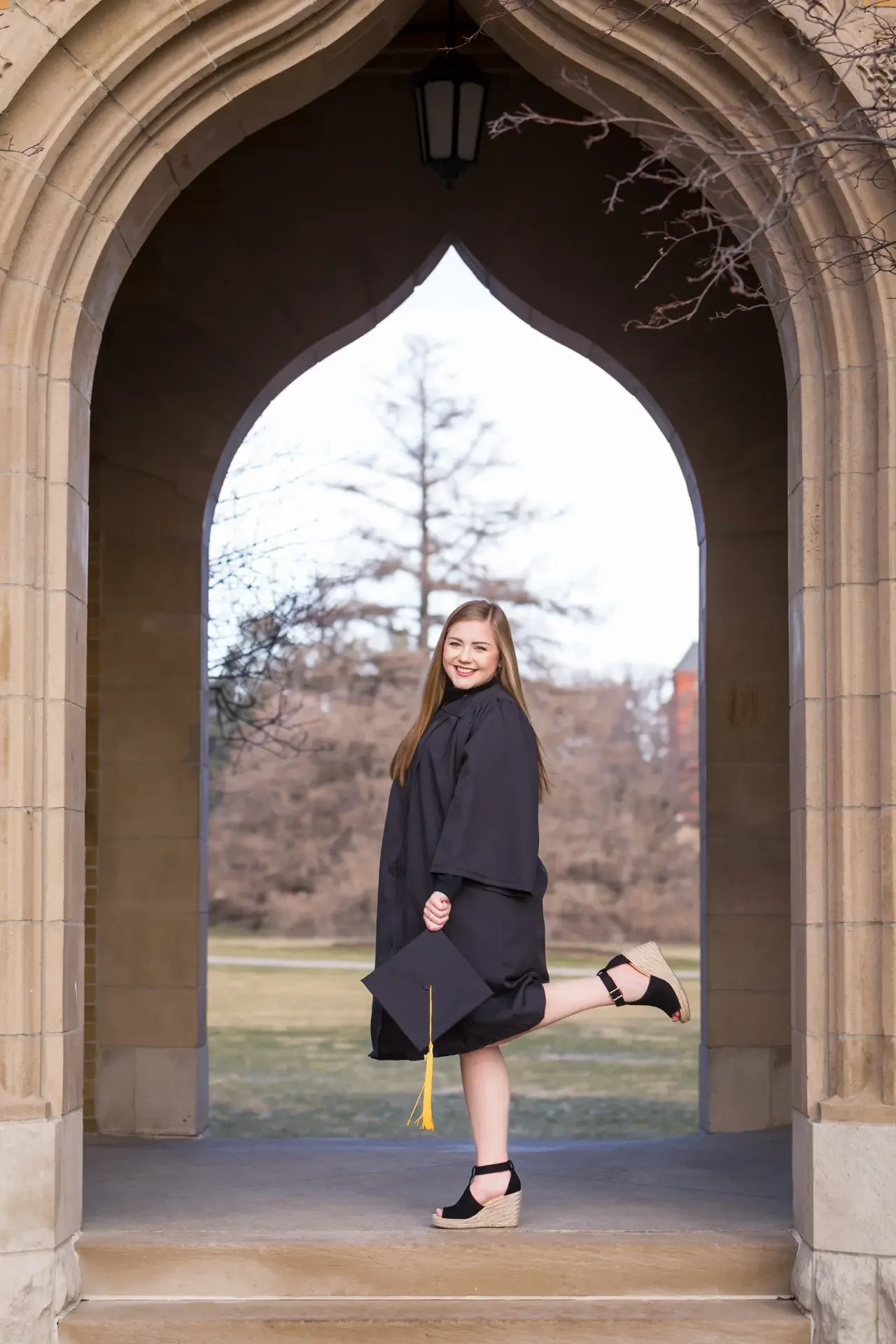 Senior girl with long hair kicking up her heel under the Campanile at ISU in Ames, Iowa.