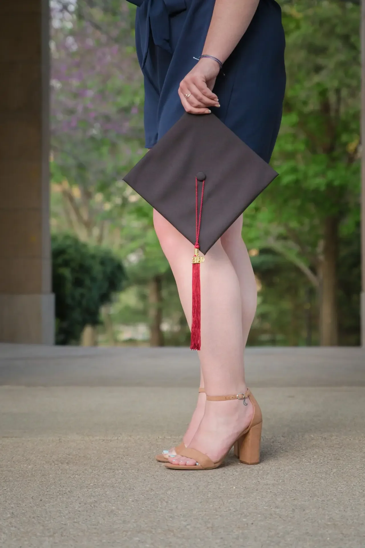 Close up of graduation cap and tassel, held at the graduate's side.