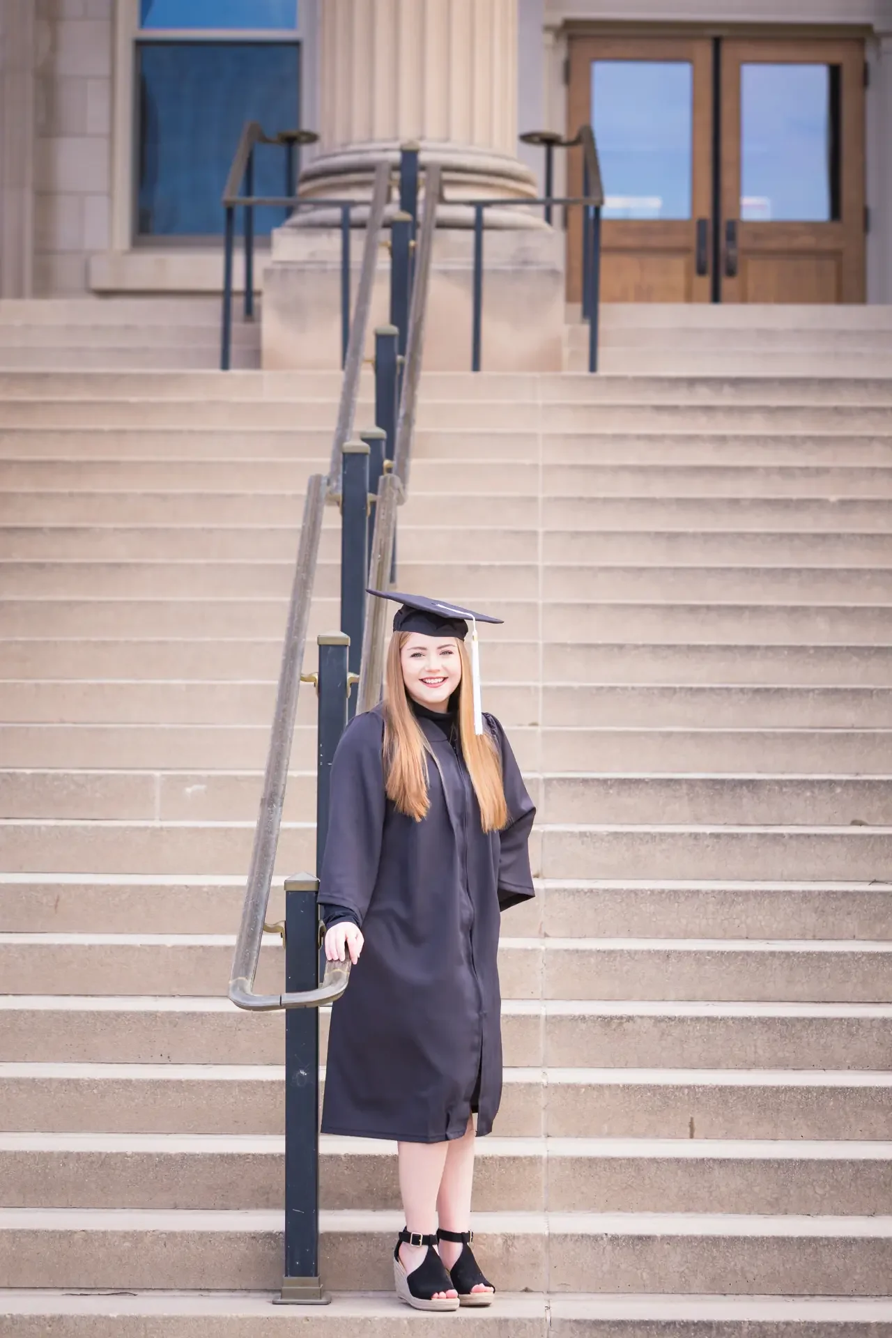 College senior wearing cap and gown, standing on the steps of Curtis Hall at Iowa State University.