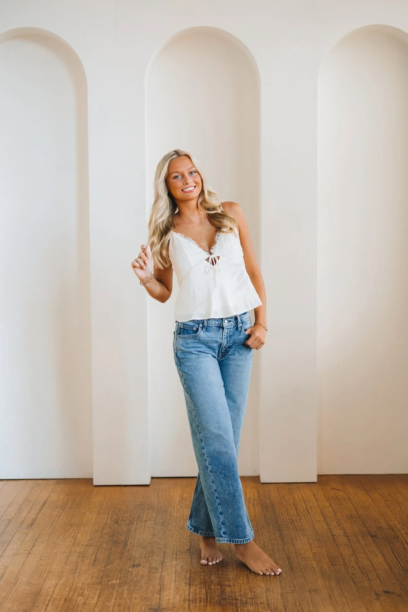 Senior girl with long blonde hair wearing a white top and blue jeans, holding her hair.