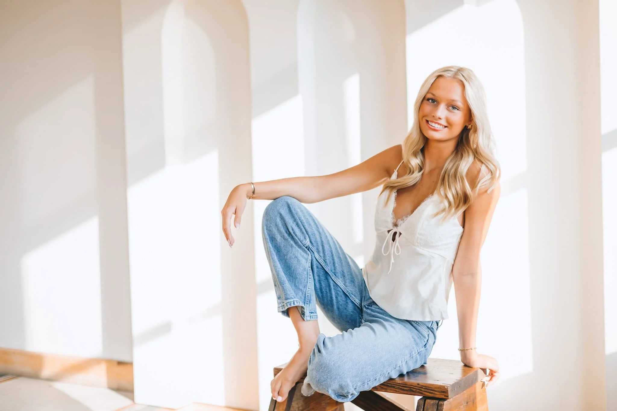 Senior girl smiling at camera, sitting on wood step ladder.