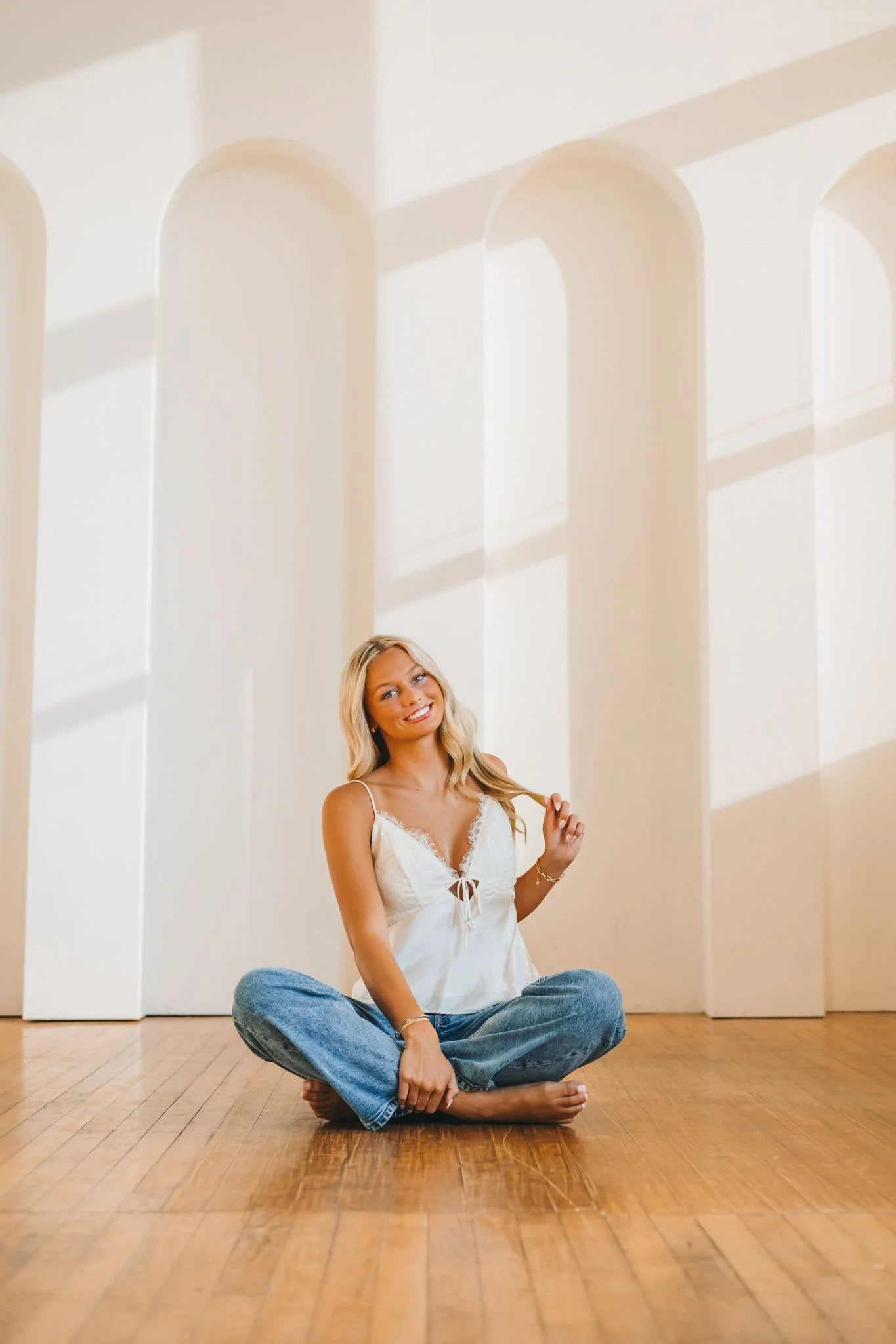 Senior girl sitting on wood floor with legs crossed, playing with her hair.