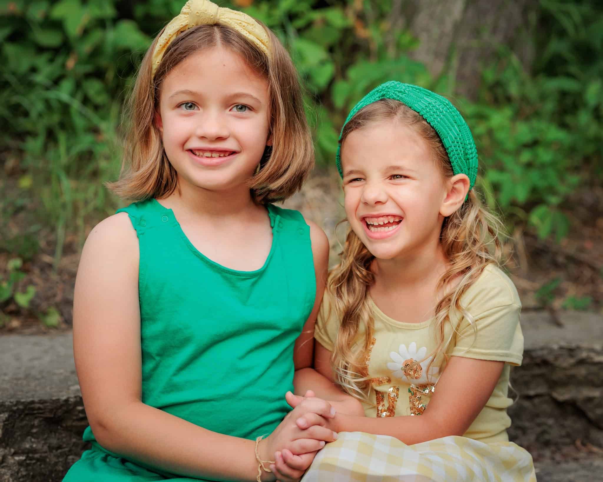 Sisters wearing green, holding hands and laughing.