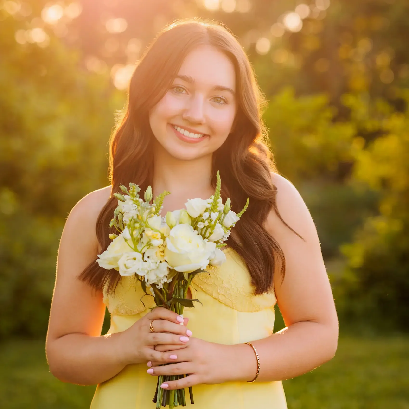 A woman in a yellow dress holding a bouquet of white flowers, outdoors at sunset.
