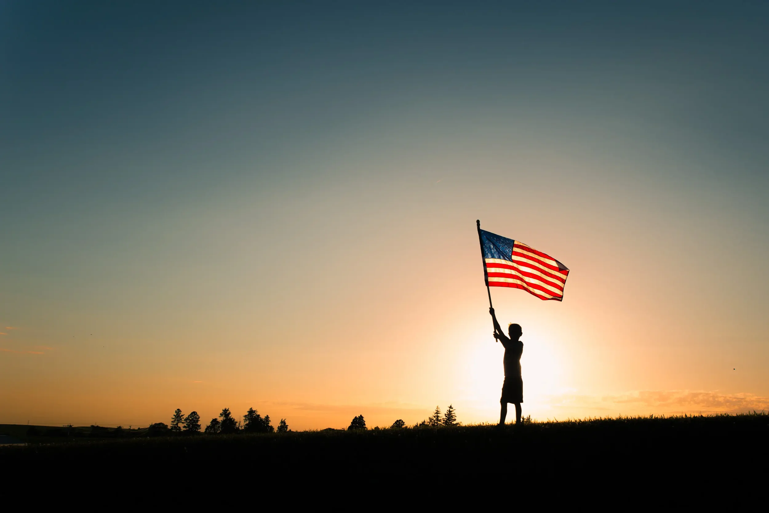 Boy silhouetted against a gorgeous sunset sky in Des Moines, holding an American flag.