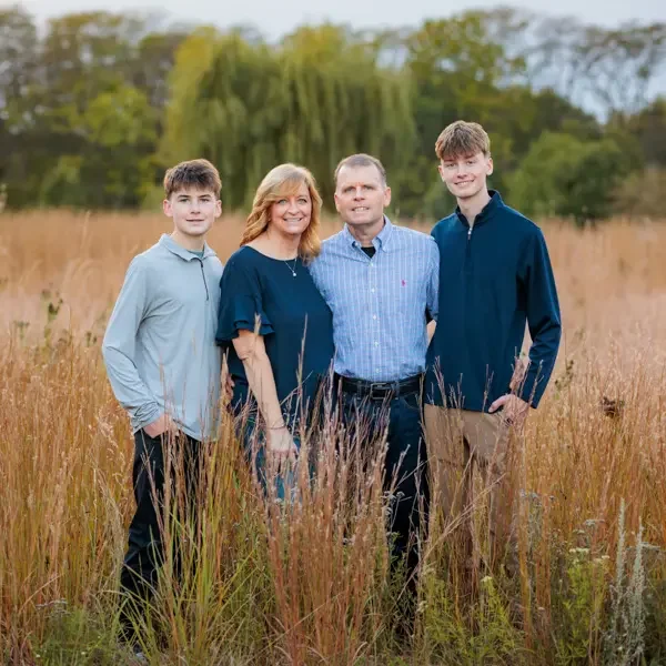 Family of 4 standing in a field of dry autumn grasses.