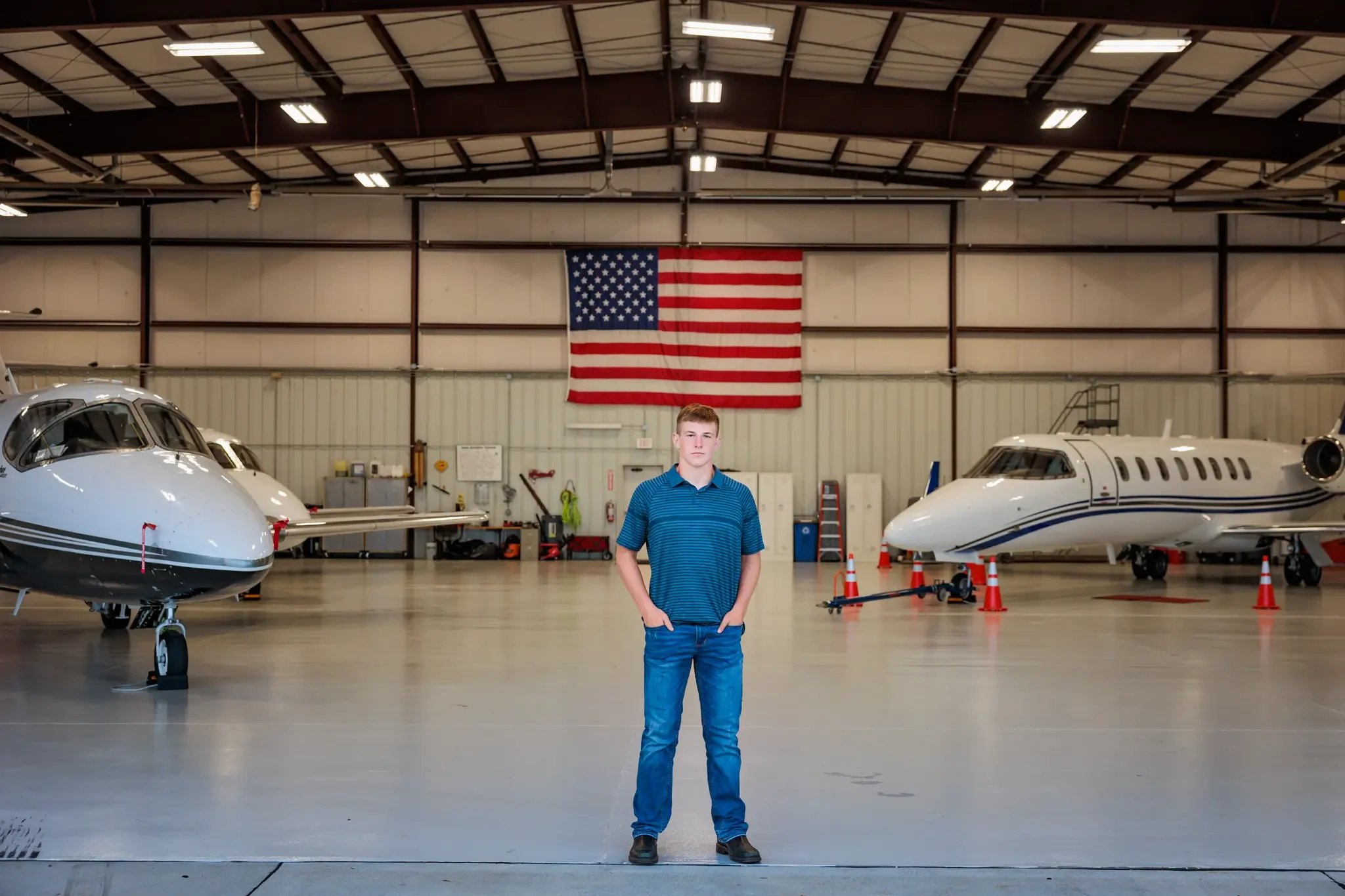 High school senior boy standing in an airplane hanger with the American Flag on the wall behind him.