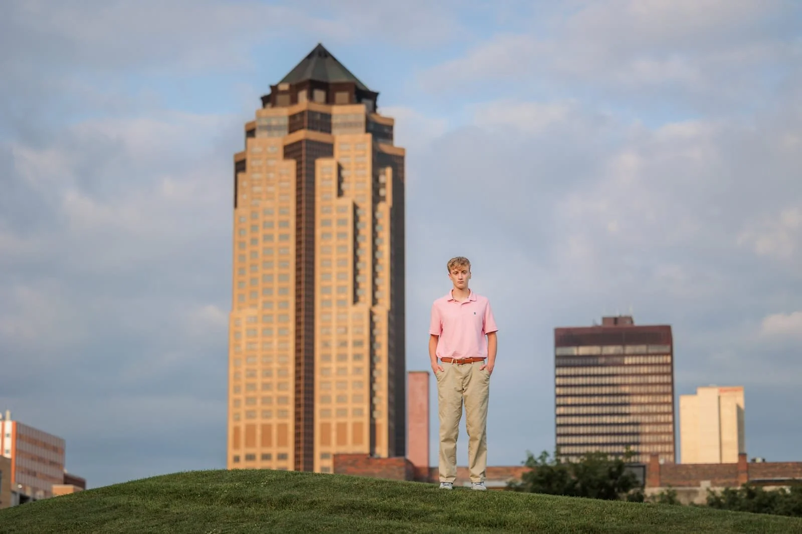Senior boy at the Papajohn Sculpture Park with the downtown Des Moines skyline behind him at sunset.