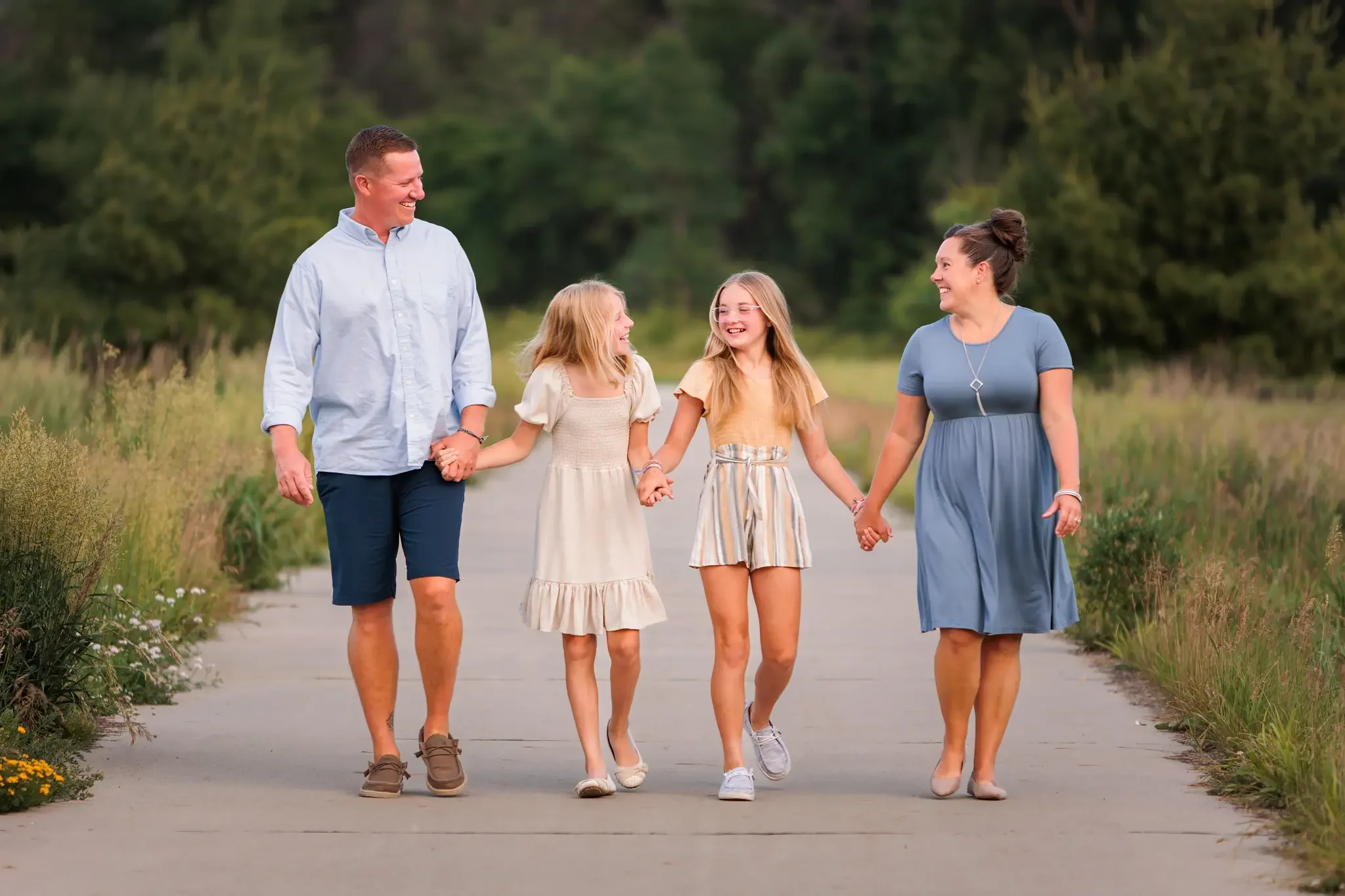 Family of 4 walking hand in hand down a paved path in the Des Moines metro area.