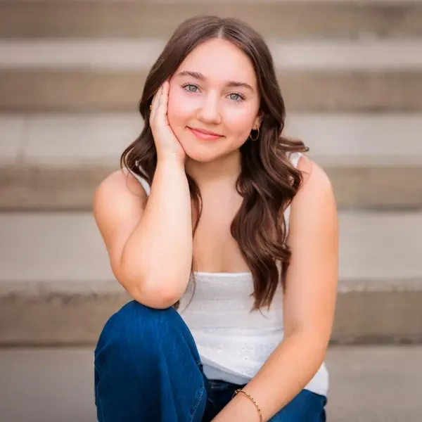 Senior girl with long dark hair with hand resting gently on face.