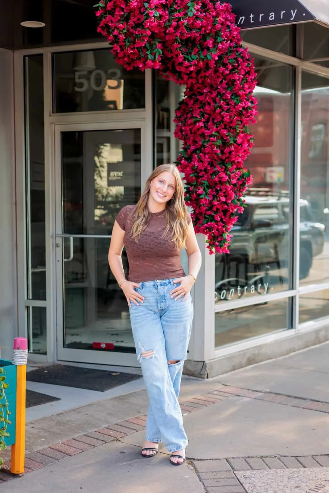 Senior girl with long dark hair wearing a brown lace top and distressed jeans.