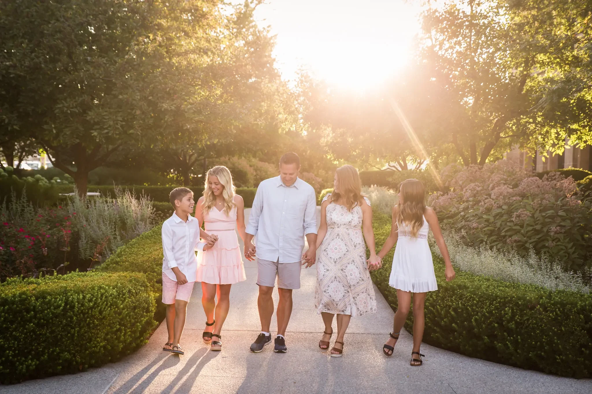 Family of 5 walking through a manicured garden holding hands at sunrise.