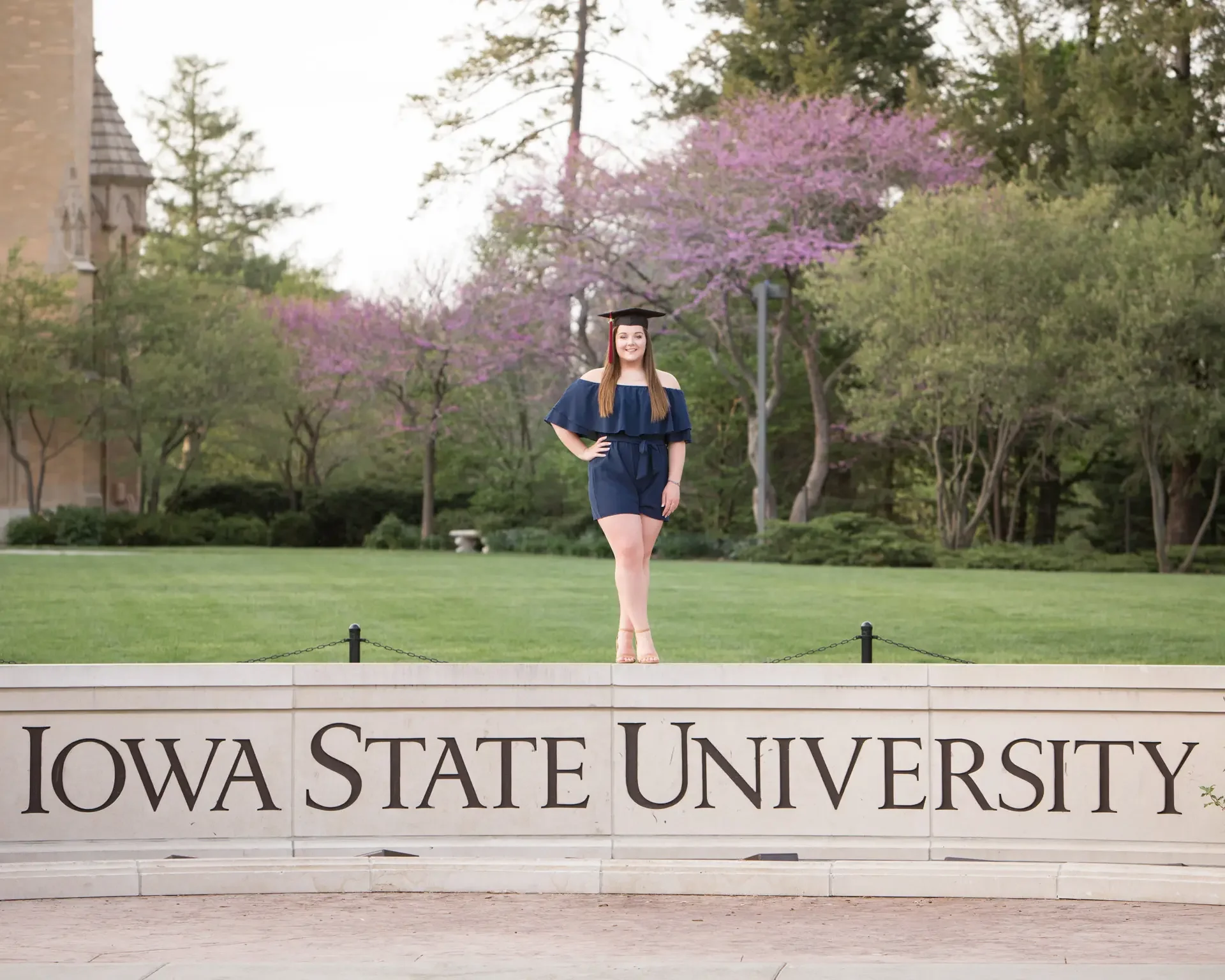 College graduate standing on top of the Iowa State University sign in Ames, Iowa.