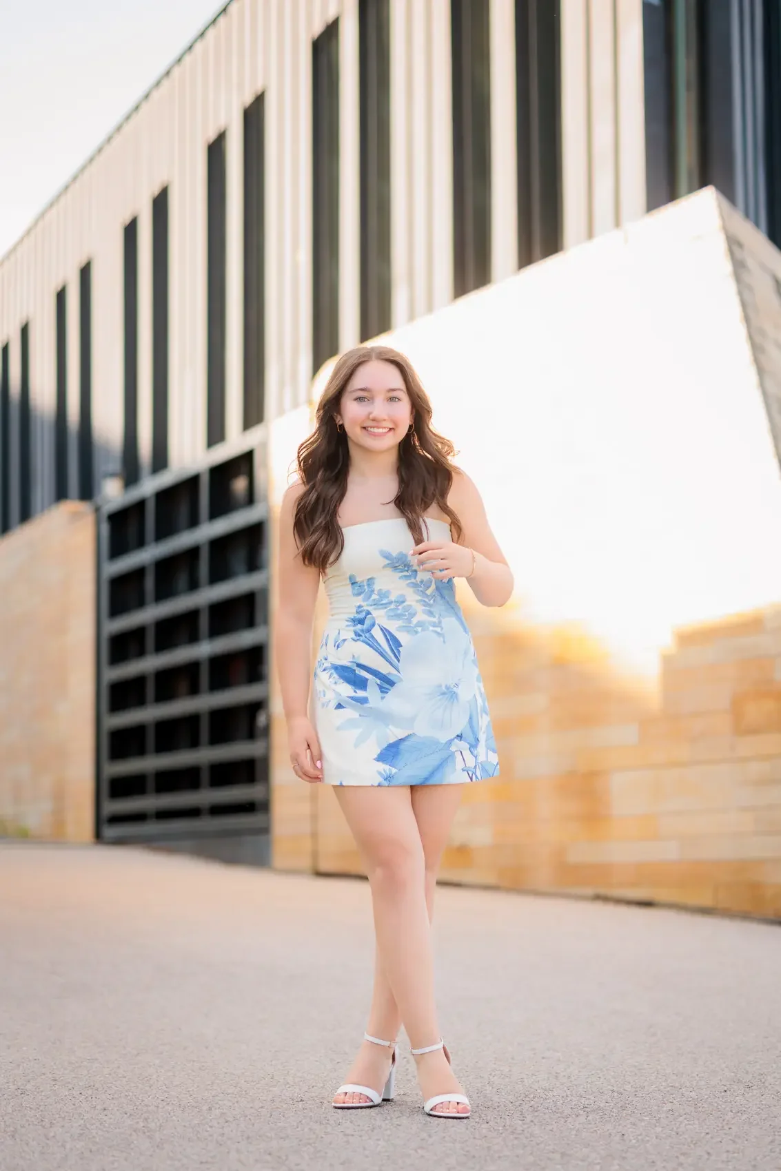 High school senior girl in a white and blue floral dress walking outdoors at sunset in Des Moines.