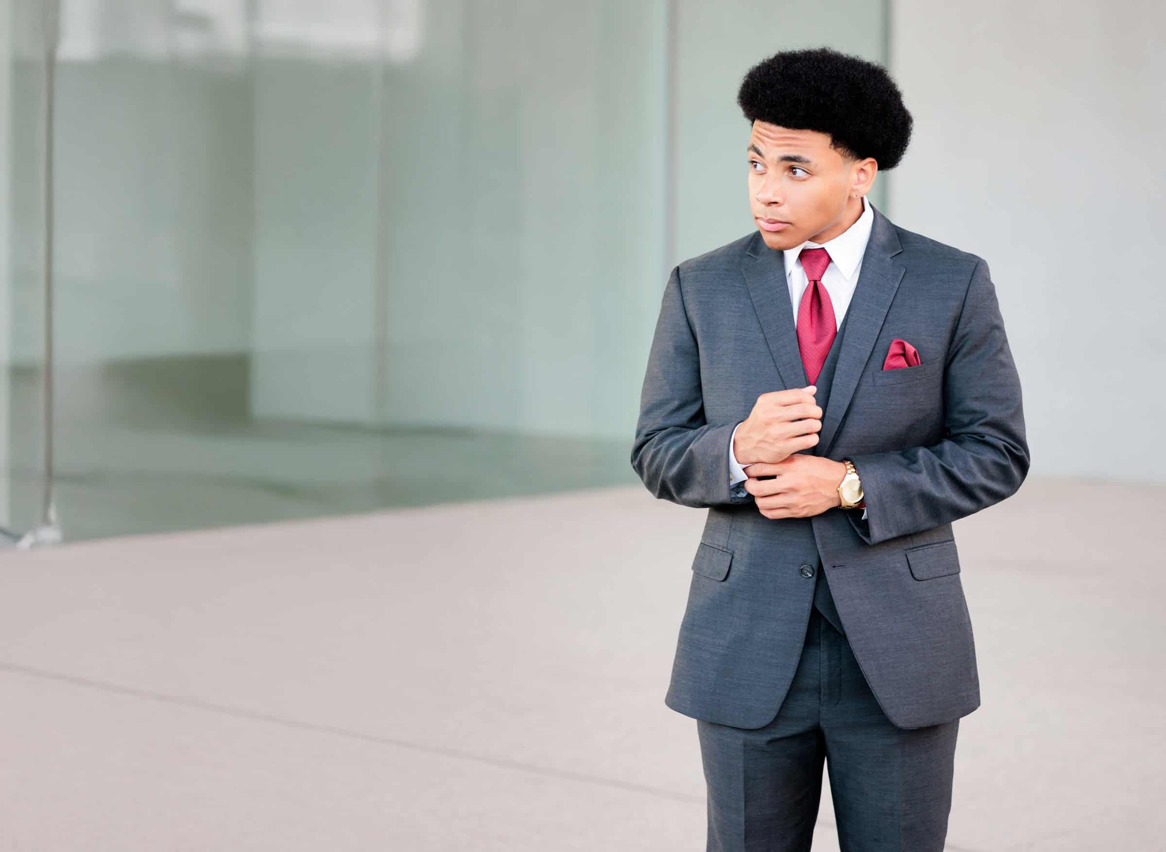 Senior boy wearing a gray suit and red tie, looking off to the side.