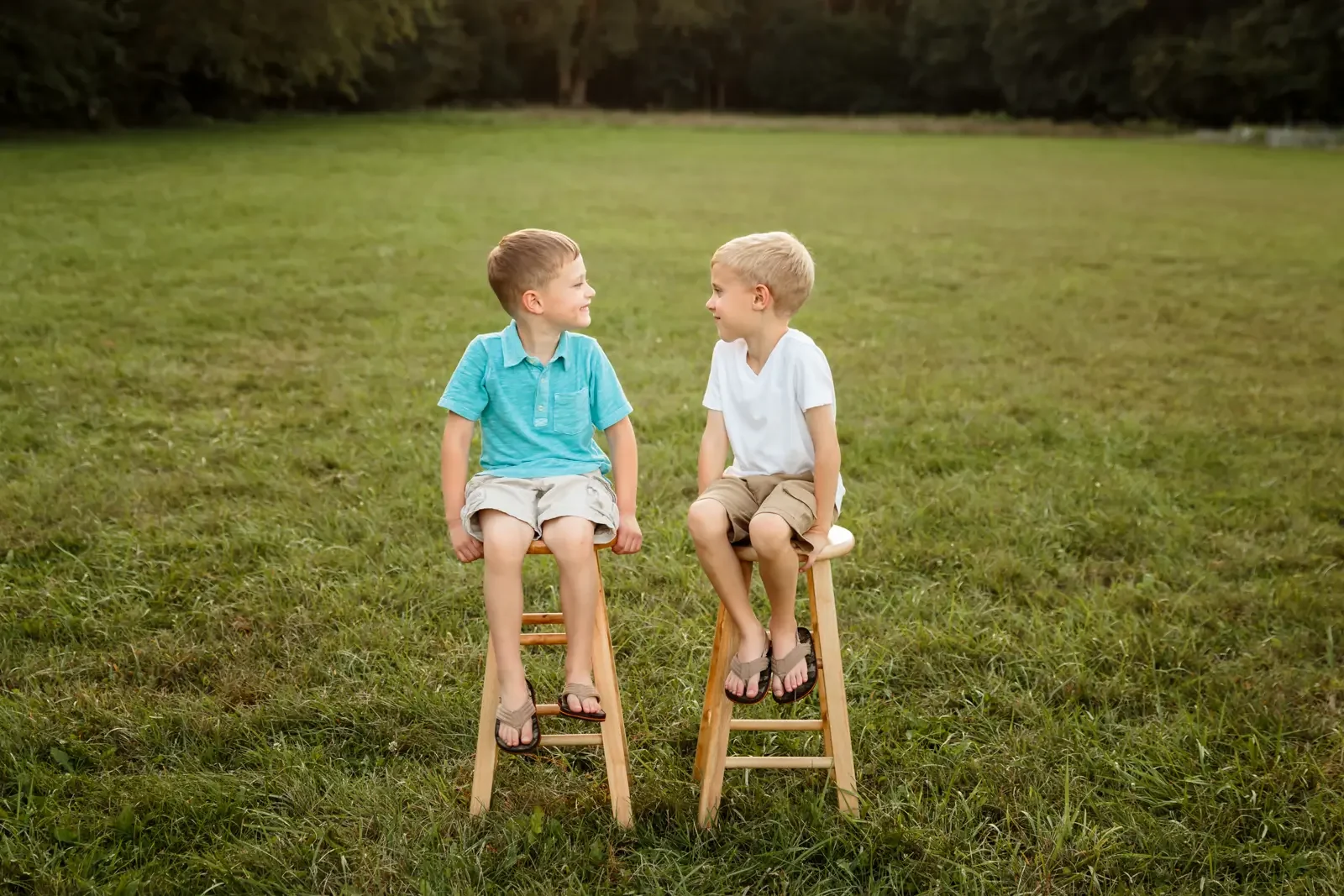Two school-aged boys sitting on stools at a park, smiling at each other, in Des Moines.