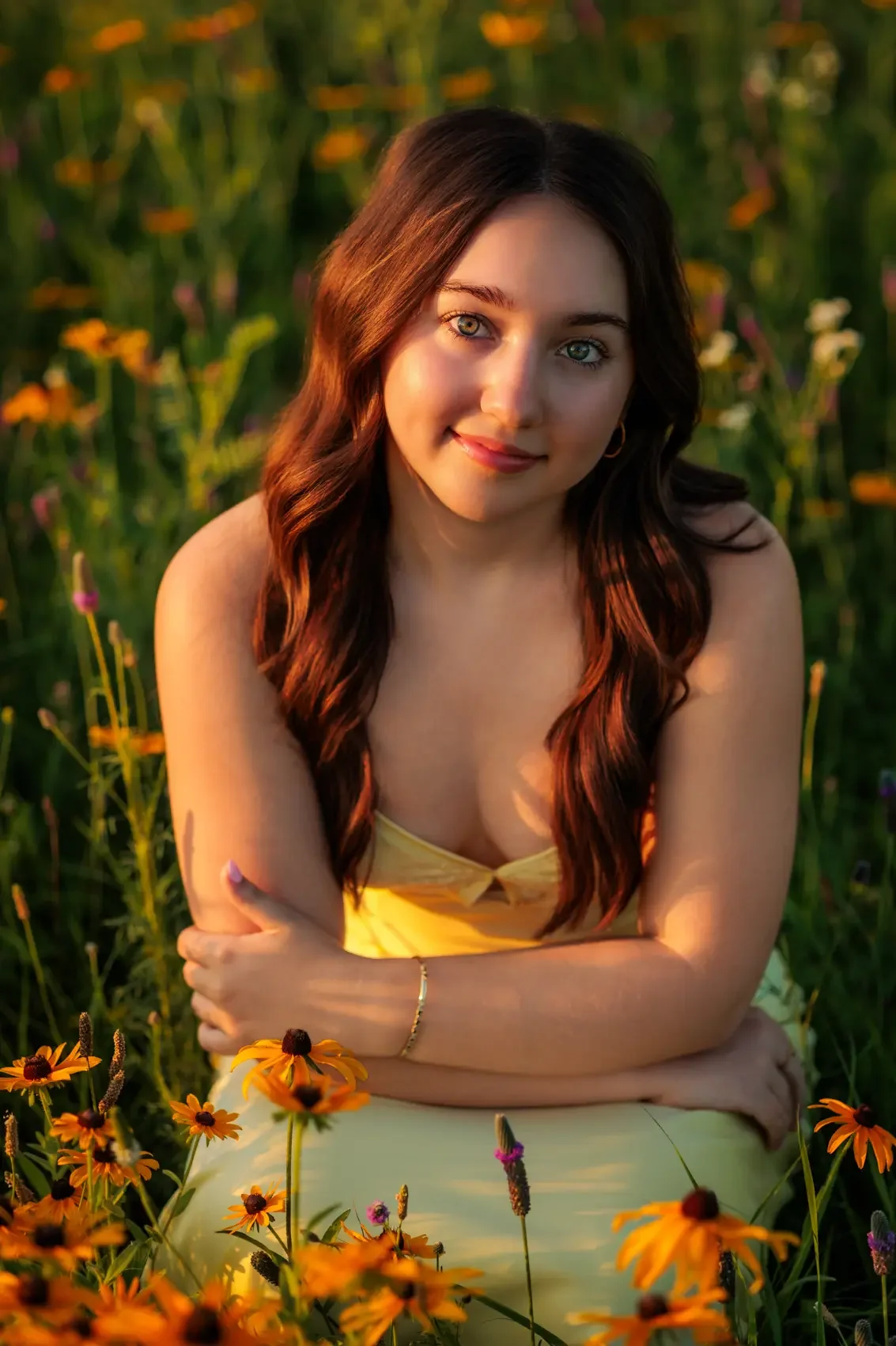 Senior girl with long brown hair and light blue eyes sitting in a field of yellow and orange flowers at sunset in Des Moines, Iowa.