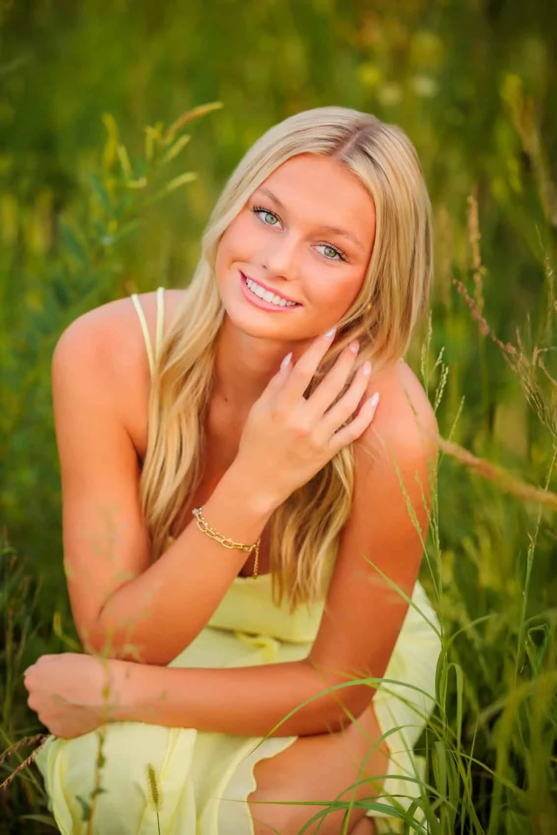 Senior girl with long blonde hair and blue eyes is smiling and posing in a grassy field during daytime. Photo by Wendy Sorensen, a Des Moines senior photographer.