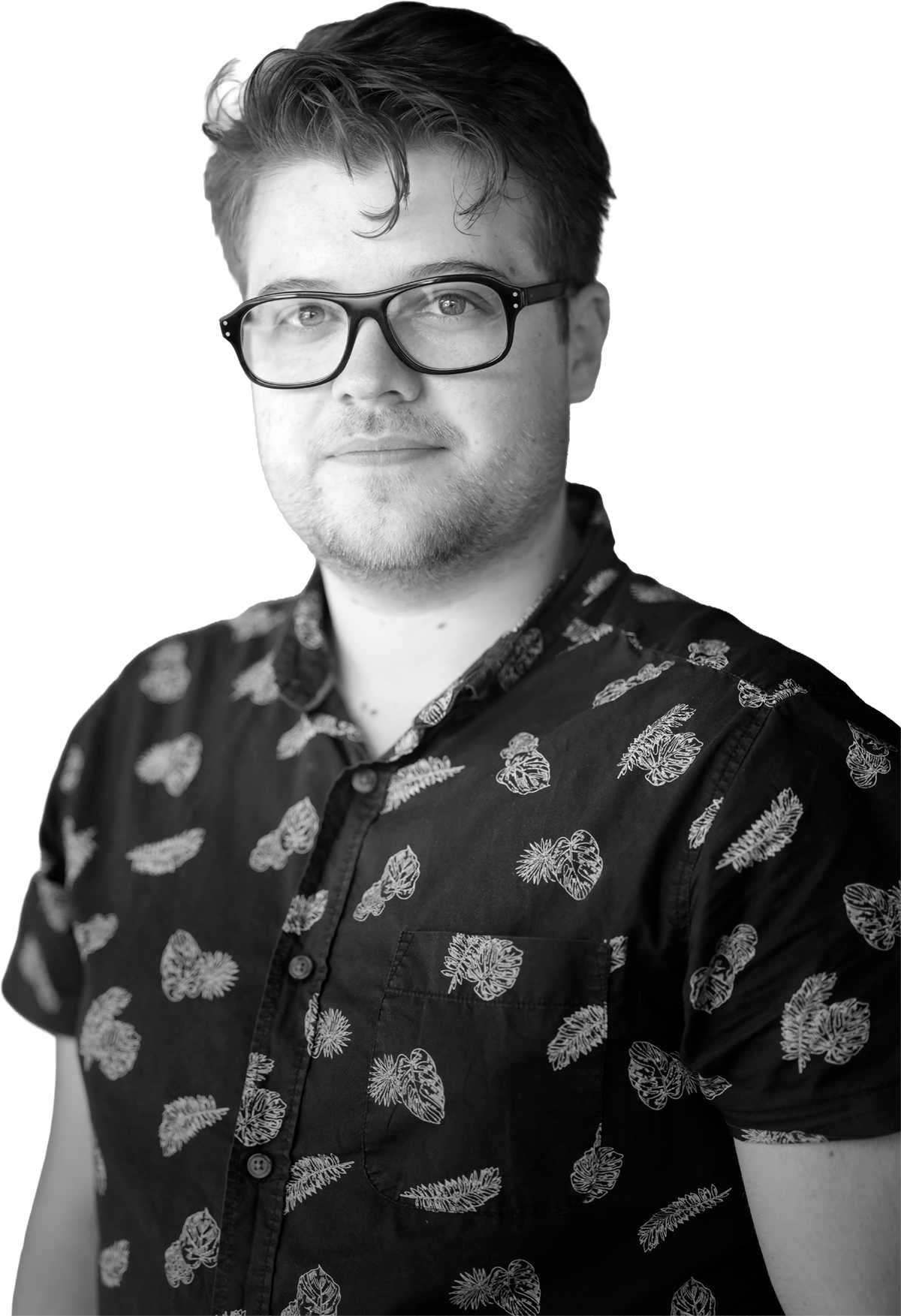 A black-and-white portrait of a young man with glasses, short wavy hair, and a light beard, wearing a short-sleeved button-up shirt with a tropical leaf print.