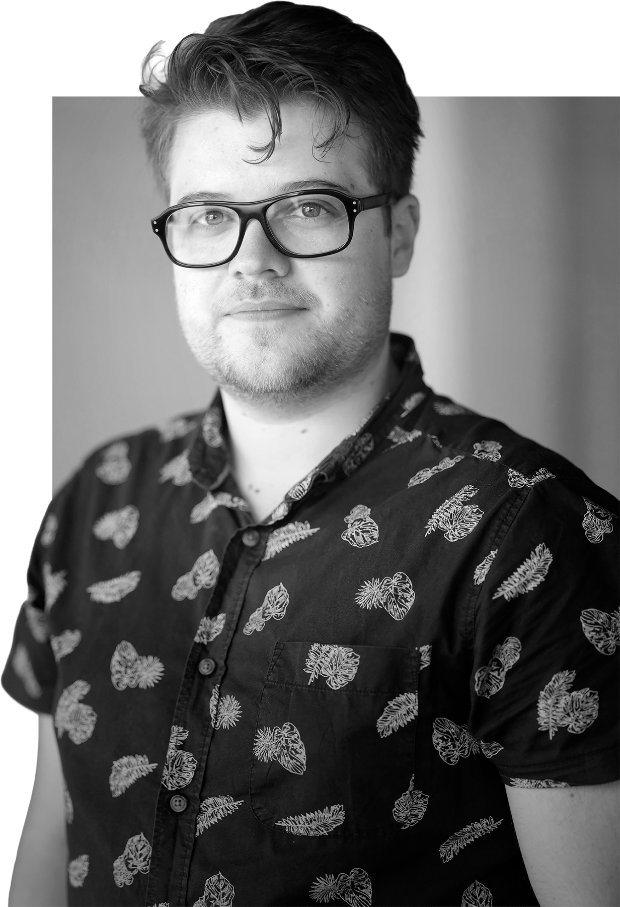 Black and white portrait of a young man wearing glasses and a patterned shirt with leafy designs, looking at the camera.