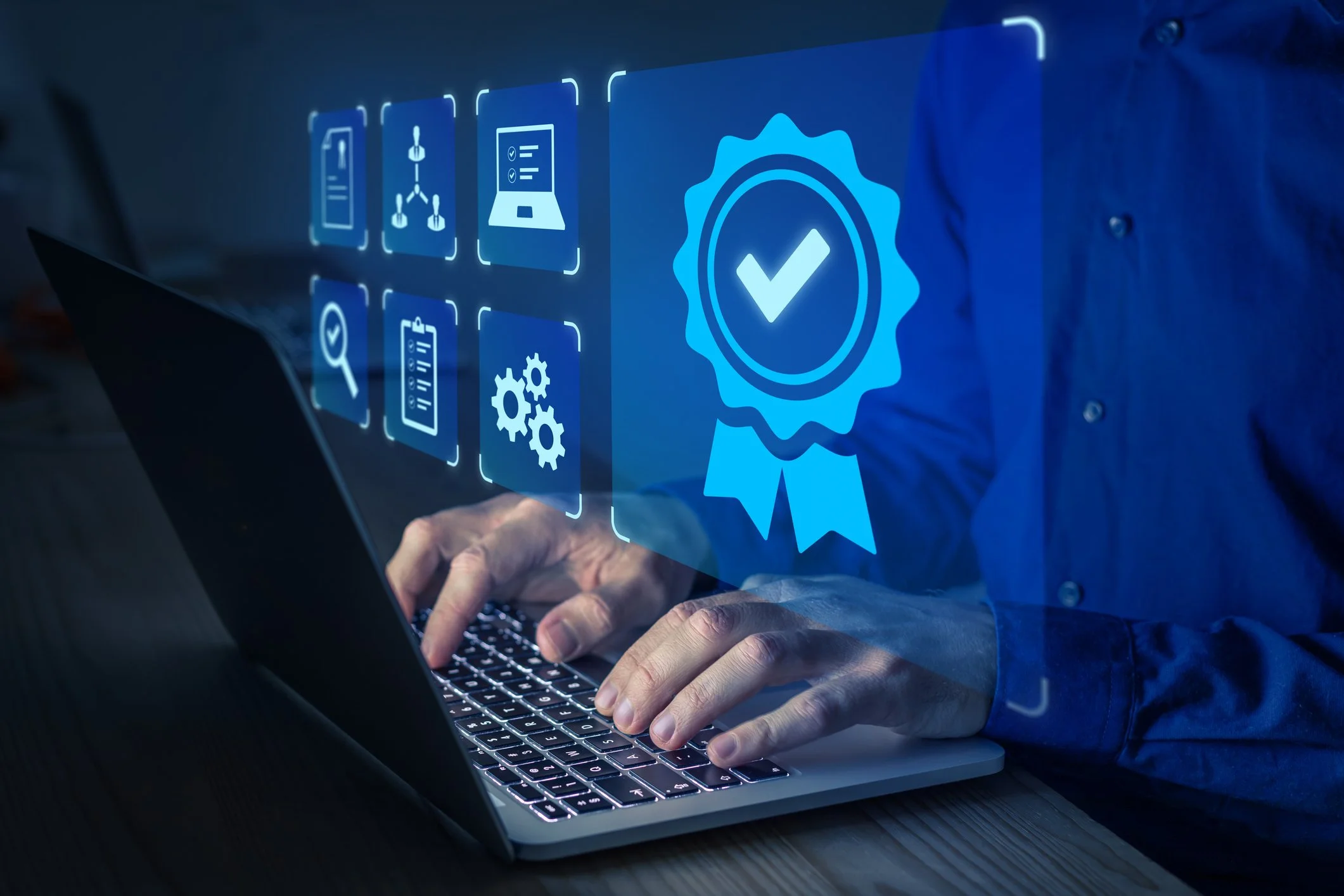 A person using a laptop with holographic icons representing certification, quality, and process management projected in front of them.