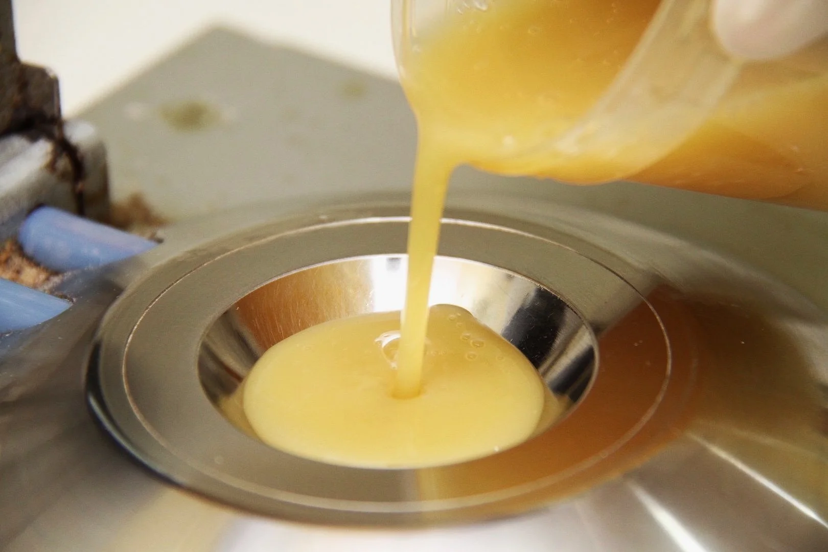 Yellow liquid being poured into a metal drain on a stainless steel sink