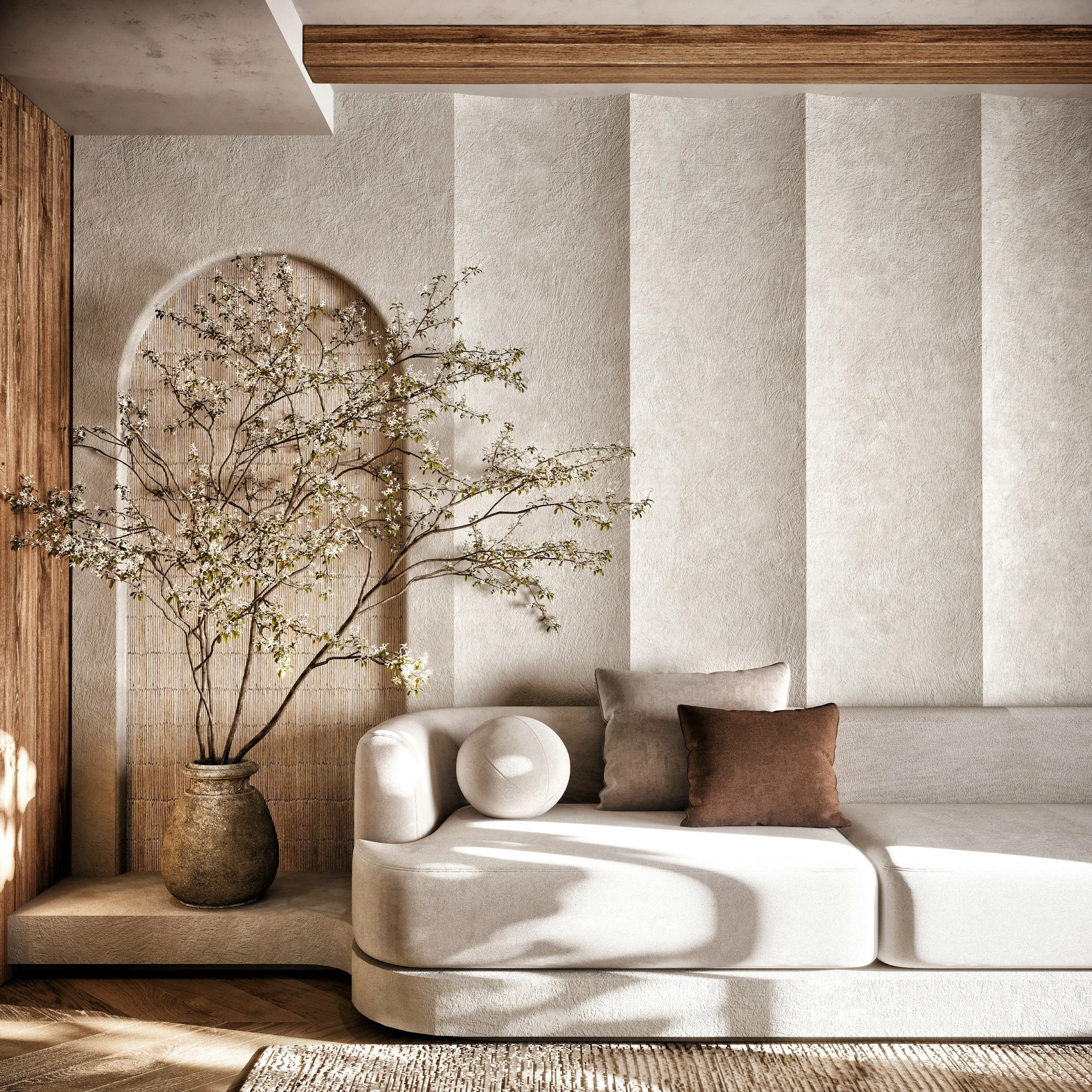 Living room corner with a beige curved sofa, two pillows (gray and brown), a round white decorative object, a large potted tree with white flowers, and a textured wall with vertical strips.