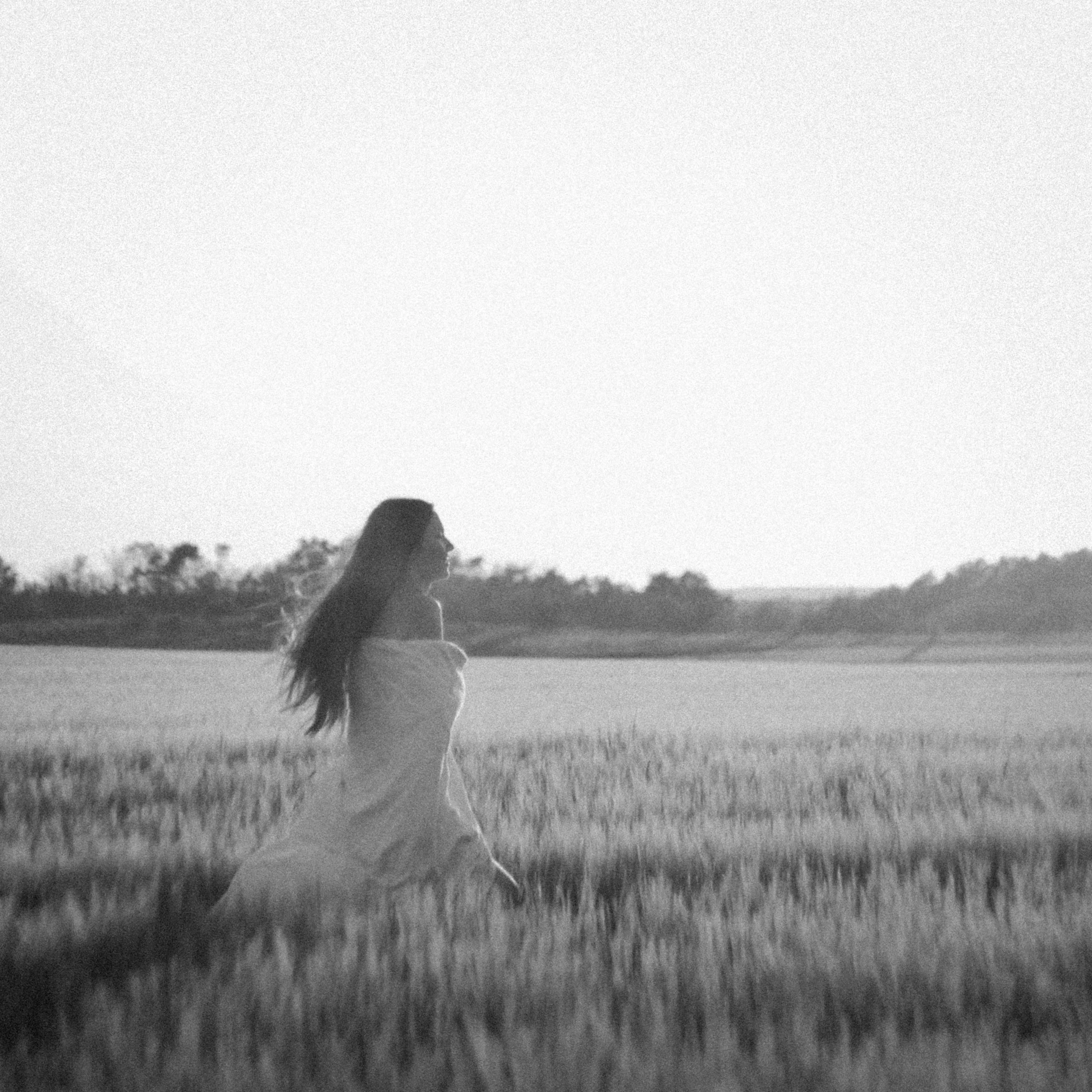 A woman in a flowing dress walking through a field during sunset or sunrise.