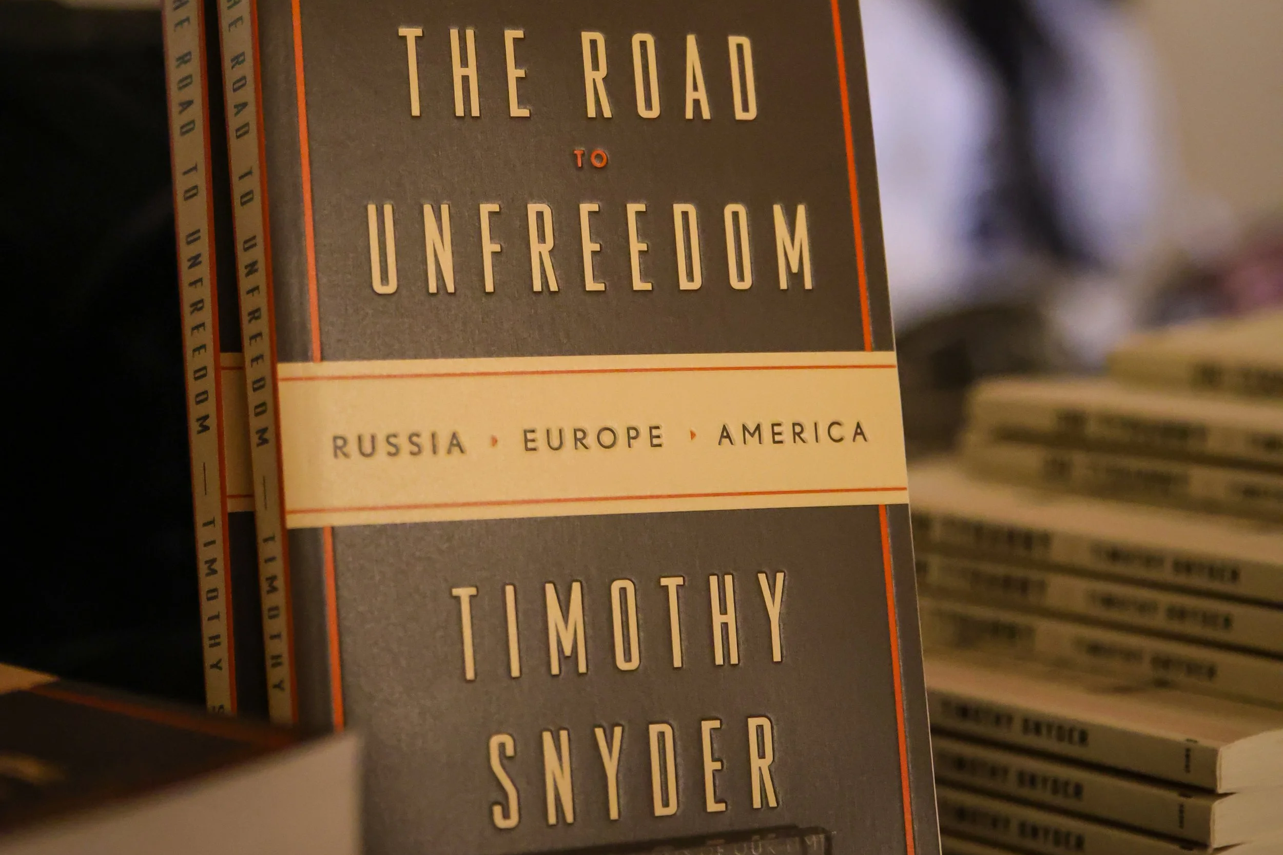 Stack of Timothy Snyder's book and "The Road to Unfreedom" book by Timothy Snyder is sitting up with other books stacked in the background.