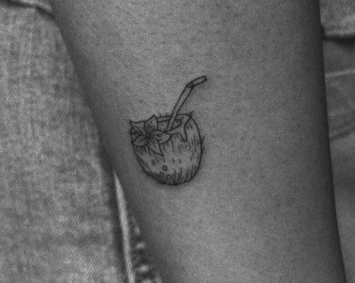 Tattoo of a coconut with a straw, partially visible on a person's thigh.